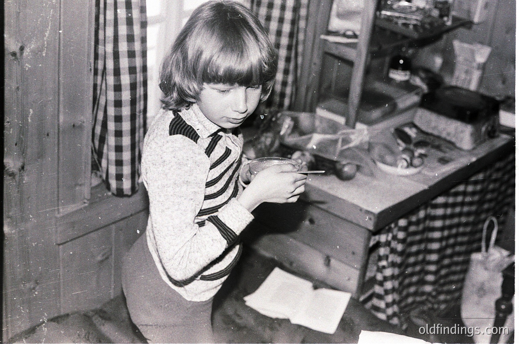 Mid-20th century kitchen scene featuring a child using a manual can opener on a vintage tin can. Wooden cabinetry and checkered curtains frame the setting. Classic 1950s–60s domestic life captured.