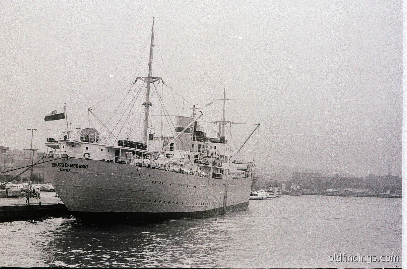 Mid-20th century passenger ship "Eduardo de Medina" docked at port, likely Bulgaria’s Black Sea coast. Noted for its sleek hull, multiple decks, and prominent funnels. Flag suggests Bulgarian registry. Urban skyline and industrial buildings in background. Ideal for maritime history, travel, and coastal architecture research.