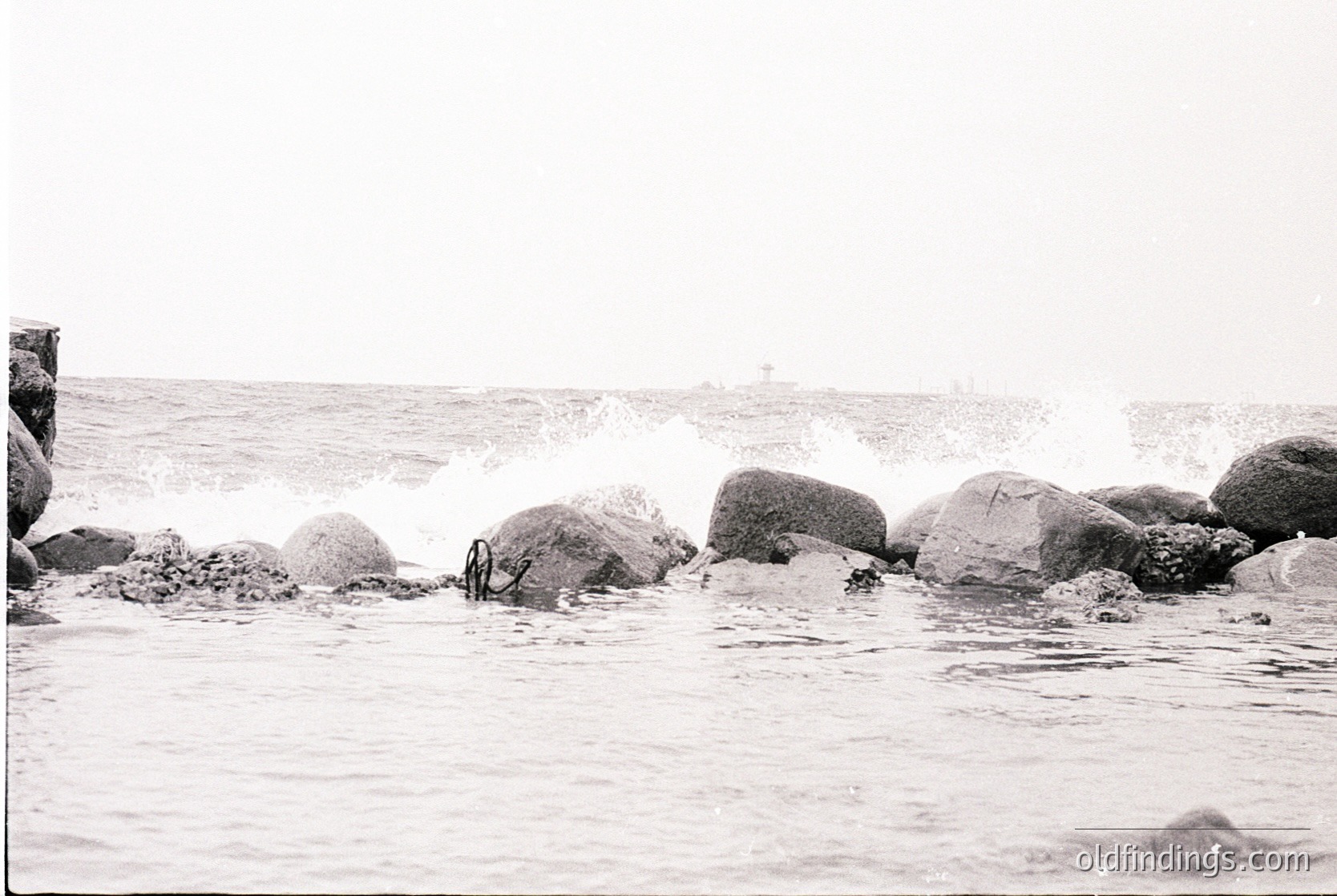 Black-and-white coastal scene featuring jagged rocks and crashing waves. Minimalist composition highlights natural textures and motion. Likely mid-20th century due to grain and framing style. Ideal for moody, atmospheric stock imagery.