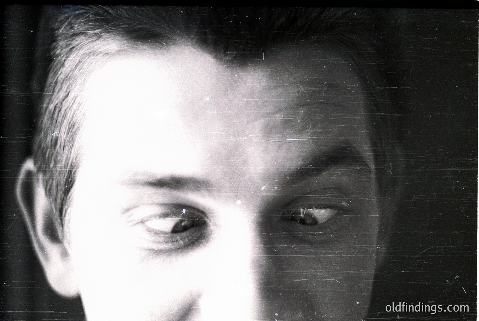 Close-up portrait of a man with short, neatly combed hair, captured in black-and-white. The grainy texture and lighting suggest a vintage or archival style, likely from the mid-20th century. His direct gaze and neutral expression evoke a timeless, candid feel.