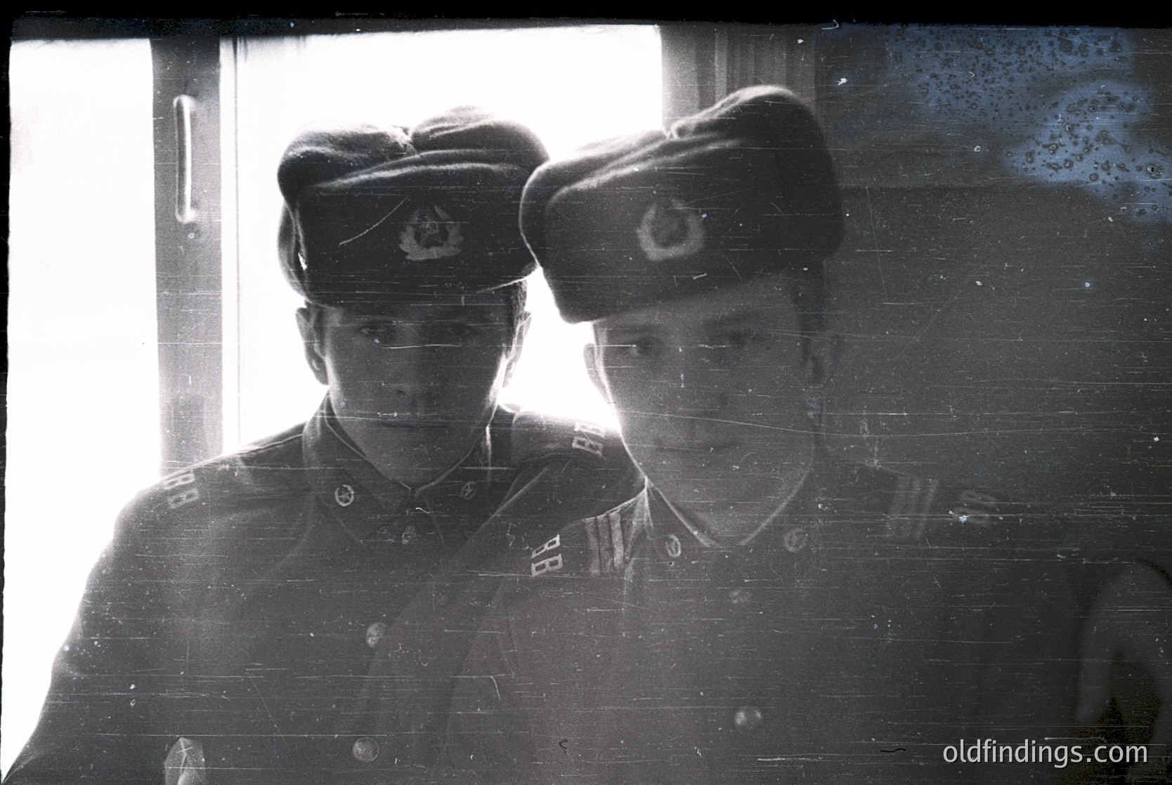 Two naval officers in mid-20th century uniforms pose indoors, reflected in a window. Distinctive red star insignia on peaked caps suggests Soviet-era Bulgarian Navy (1940s–1980s). Rank patches indicate senior enlisted or junior officer status. Grainy sepia tone enhances vintage aesthetic.