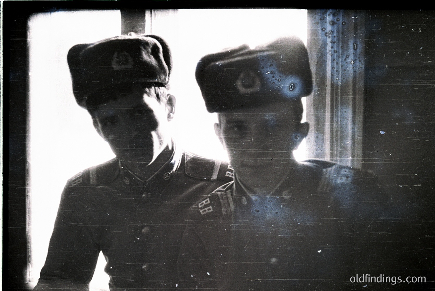 Vintage sepia-toned portrait of two uniformed individuals in Soviet-era military caps, likely 1940s–1950s. Distinctive red star insignia and shoulder patches suggest Eastern Bloc affiliation. Taken indoors near a window, framing suggests a candid or staged military setting.