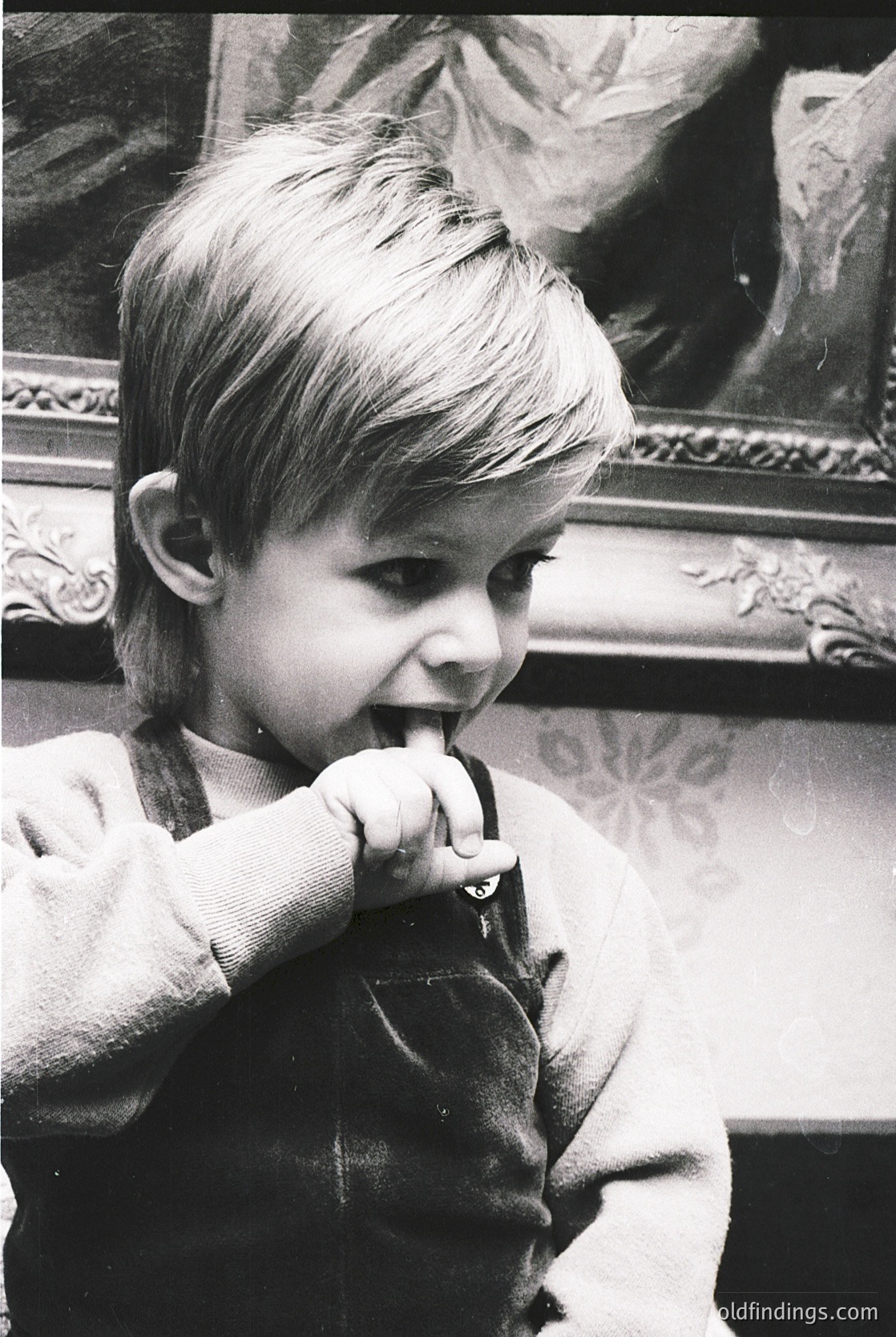 Young child in vintage sweater brushing teeth indoors, framed classical painting in background. Mid-20th century domestic scene, likely Western Europe or North America.