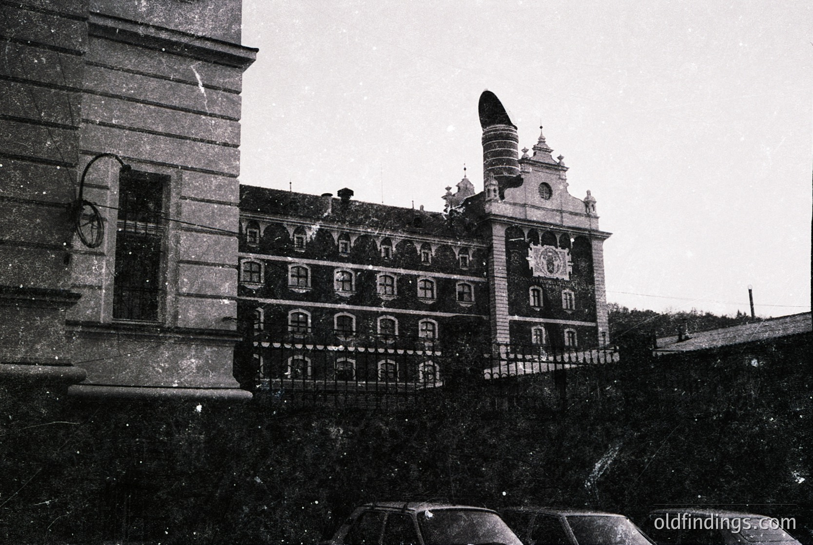 Historic grand building with ornate Baroque façade, featuring a central clock tower and decorative stonework. Snow blankets rooftops and ground, suggesting winter. Black-and-white vintage aesthetic.