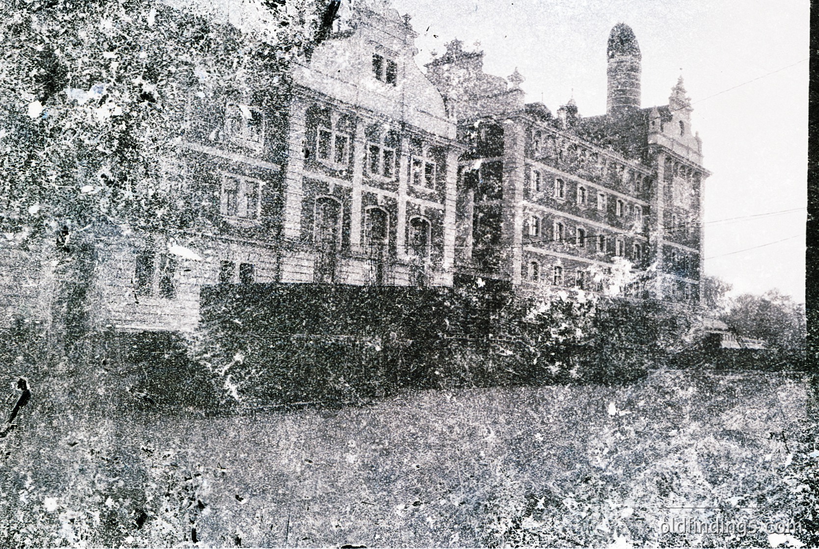 Grand neoclassical building with symmetrical façade, tall windows, and central tower—likely a historic hotel or institutional structure. Lush greenery and mature trees frame the scene, suggesting a landscaped estate. Early 20th-century architectural style with stone or brick construction.
