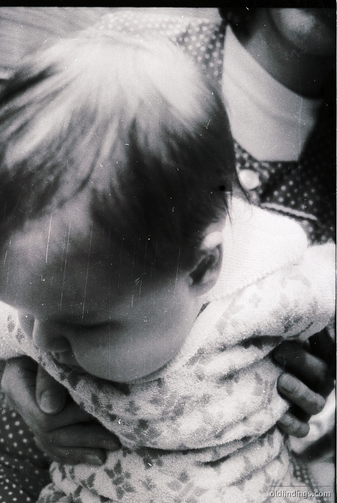 Close-up of a child in mid-laugh, sunlight streaming through hair. Patterned fabric (likely a dress) with subtle polka dots. Vintage black-and-white film grain suggests mid-20th century (1940s–1960s). Candid, intimate moment captures youthful joy.