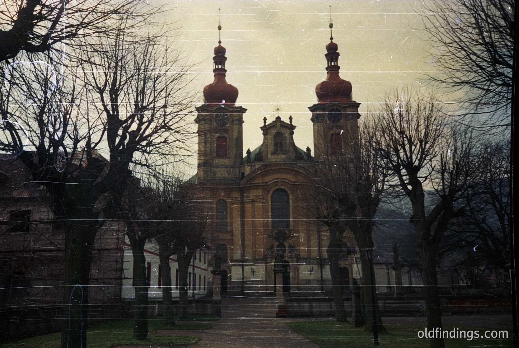Baroque-style church with twin domed towers and ornate façade, framed by bare winter trees. Likely Eastern European architecture, possibly . Vintage sepia tone suggests historical or archival use.
