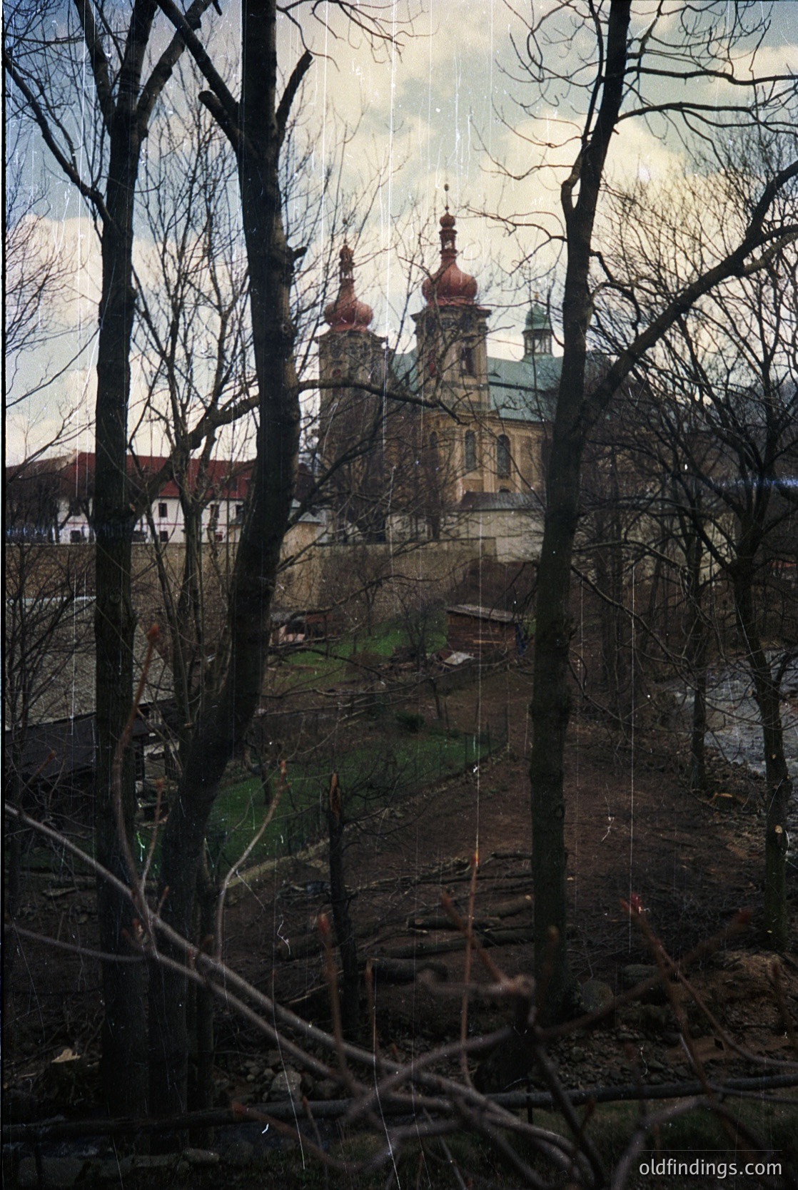 Baroque-style church with twin red-domed towers framed by winter trees. Architectural details include ornate facades and a central bell tower. Likely Eastern European, possibly . Dramatic lighting enhances texture and mood.