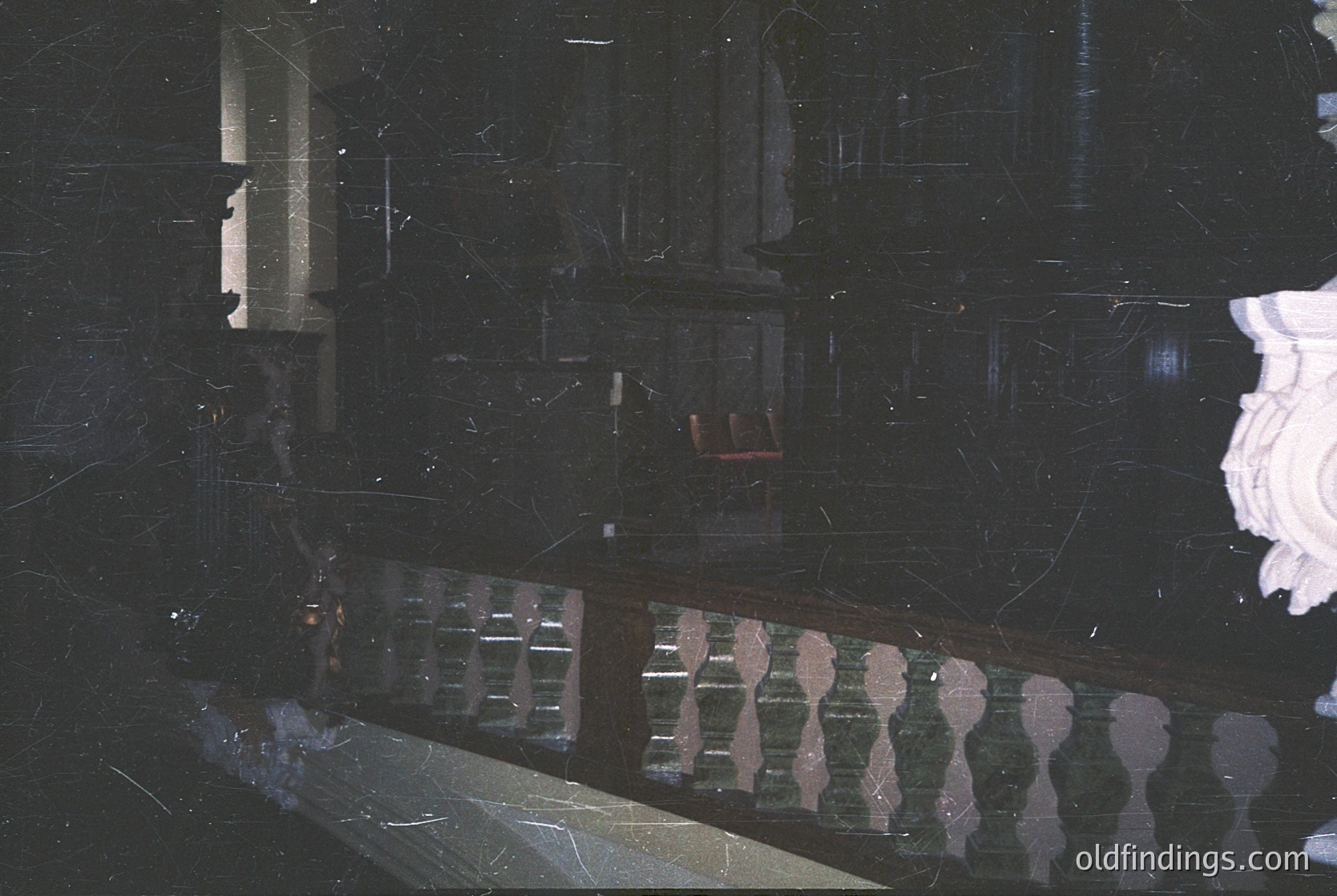 Vintage black-and-white photo of a grand, dimly lit interior staircase with ornate wrought-iron railings and marble steps. Reflections reveal architectural symmetry and a central chandelier. Likely a public building or hotel from the early-to-mid 20th century.