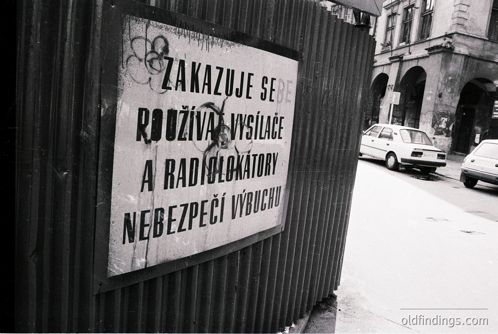 Czech warning sign prohibiting fireworks and radio detectors near exits for safety. Urban street scene with vintage car, likely 1980s–1990s Prague.