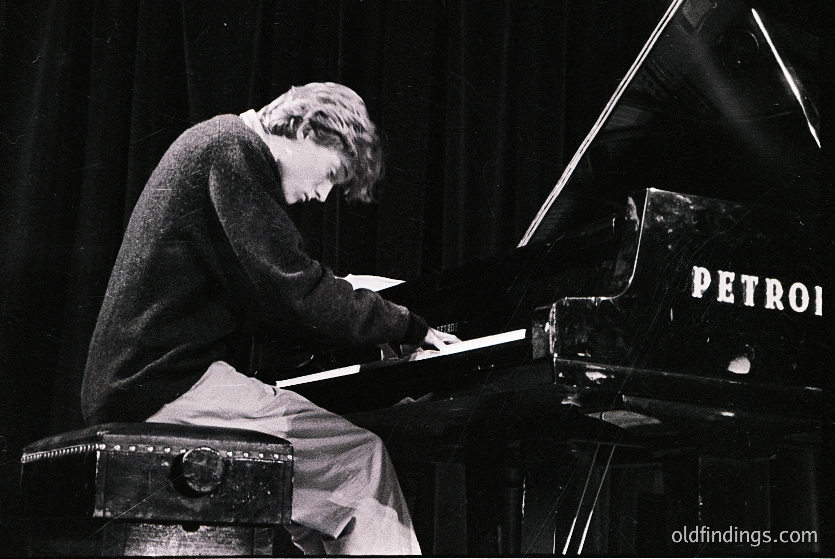 Black-and-white portrait of a pianist seated at a **Petrof upright piano** on stage, engrossed in performance. Mid-20th century attire suggests **1950s–1960s** era. Stage lighting and suitcase prop hint at touring or concert setting.