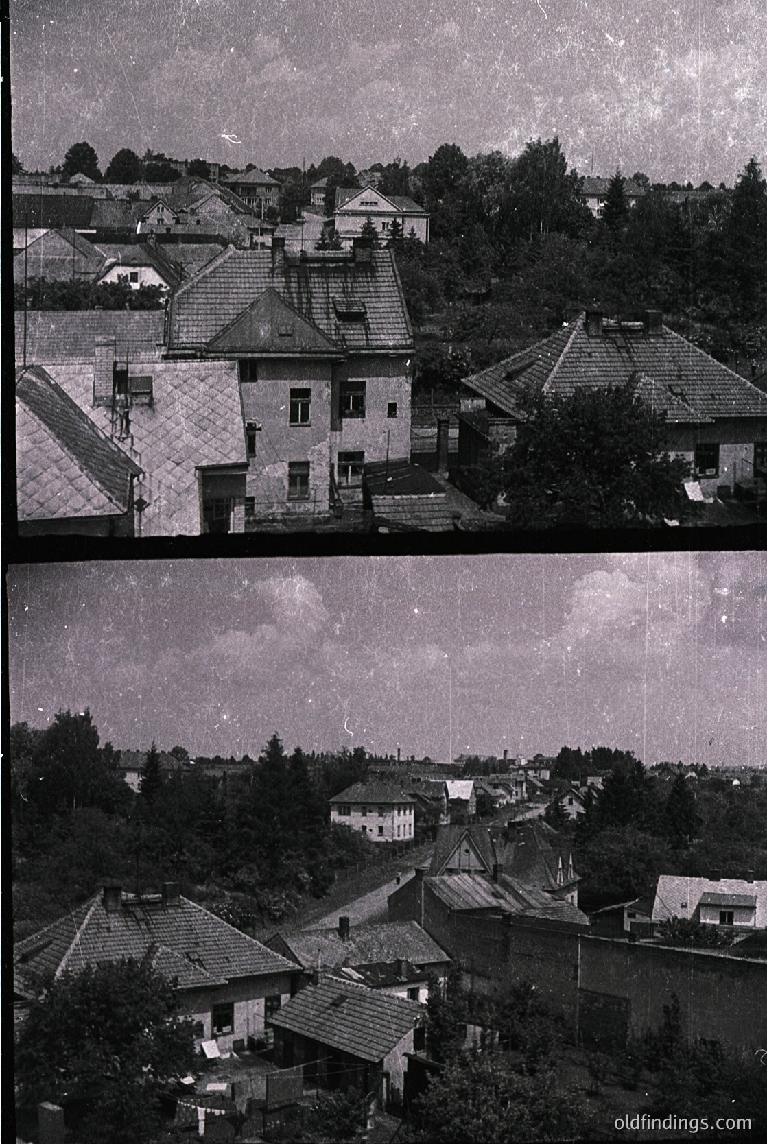 Vintage aerial view of densely packed residential rooftops with slate and tiled roofs, likely Eastern European. Mid-20th century architecture with mixed construction styles, including brick and plaster facades. Vegetation and trees frame the horizon, suggesting a hilly or suburban area.