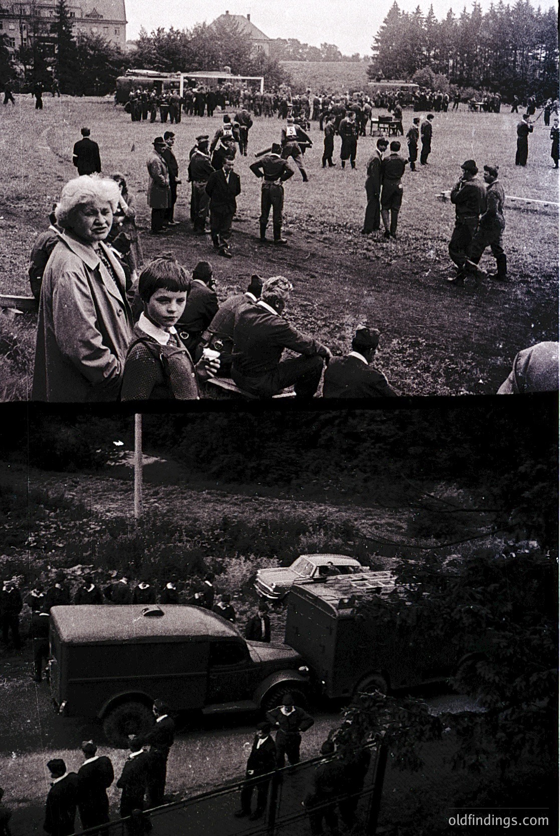 Mid-20th century outdoor gathering in a grassy field with vintage cars and uniformed individuals. Crowd includes adults and children, some seated on grass, others standing. Classic black-and-white style suggests 1950s–1960s era. Possible sports event or public assembly.
