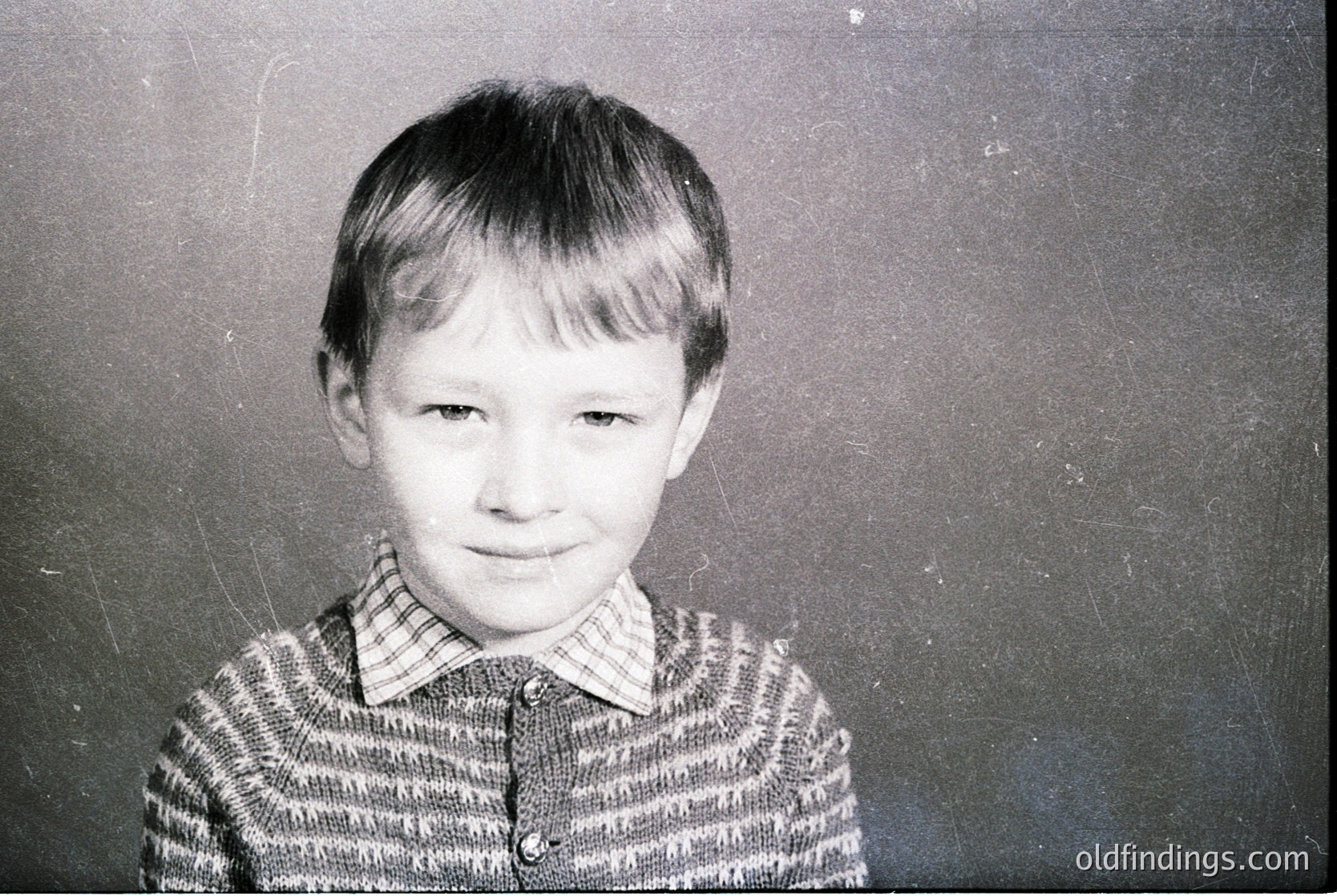 Black-and-white portrait of a young boy in a striped sweater, likely mid-20th century. Plain backdrop suggests school or studio setting. Distinctive hairstyle and clothing reflect 1950s–1960s Western/European style.