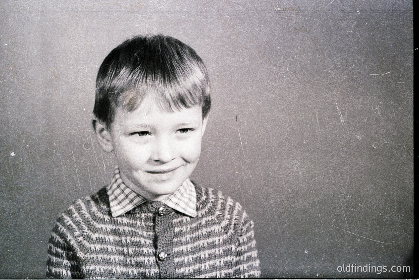 Vintage black-and-white portrait of a young boy in a striped sweater, mid-20th century style. Plain backdrop suggests studio or school setting. Candid smile captures innocence and warmth.