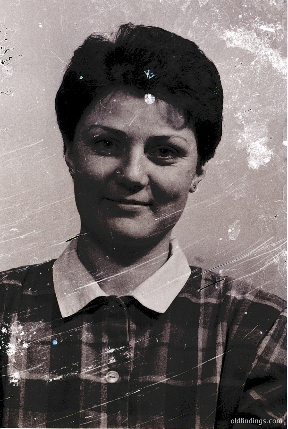 Vintage black-and-white portrait of a woman in a plaid blouse, short hairstyle with bangs, and a single brooch. Likely mid-20th century (1950s–1970s) studio portrait.