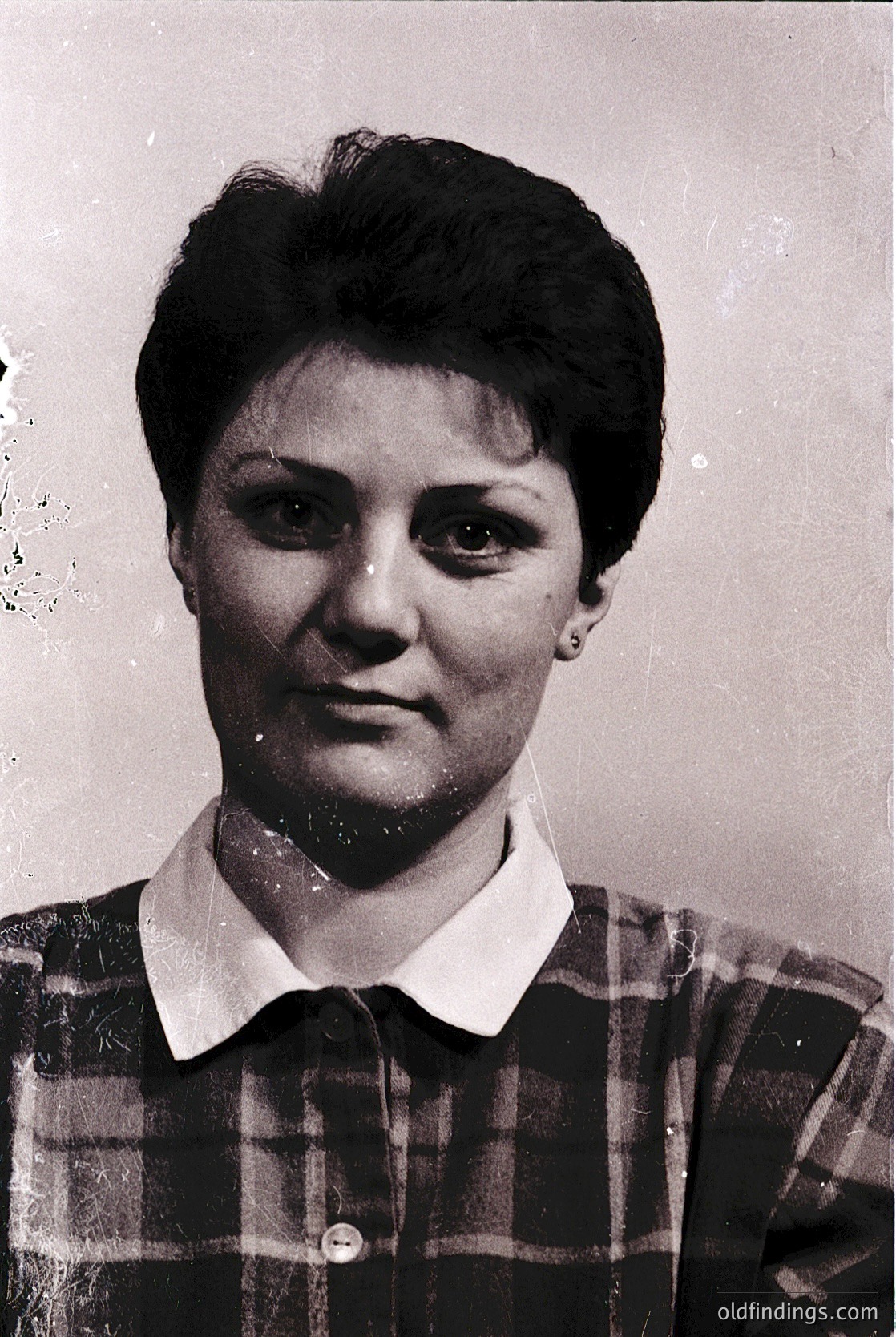 Black-and-white portrait of a woman in a plaid blouse, short hair, and minimal jewelry—likely a 1970s–1980s identification or school photo. Plain background suggests institutional use.