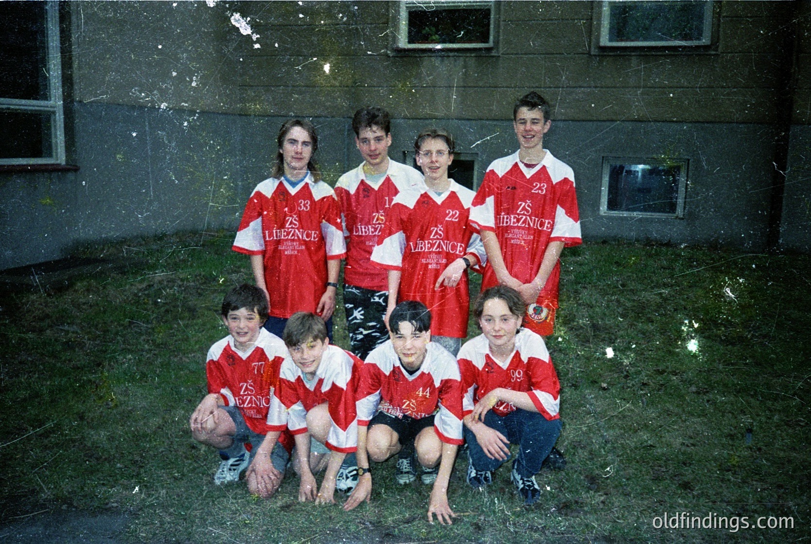 Vintage team photo of **ZS Treznice** soccer players, 1990s. Seven young men in red-and-white striped jerseys pose outdoors against a weathered concrete wall. Back row kneels; front row squats. Grass and worn pavement suggest a local field.