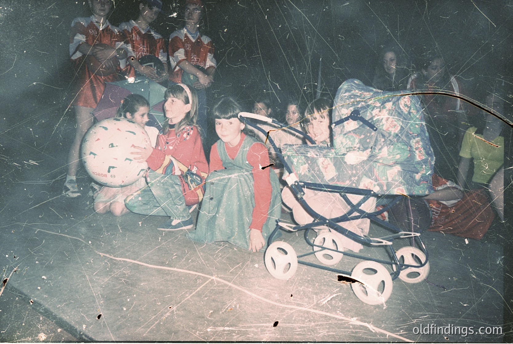 Vintage indoor gathering with children seated on floor, surrounded by luggage and a vintage stroller. Blurred, grainy quality suggests mid-20th century (1950s–1970s). Possible travel or displacement setting.