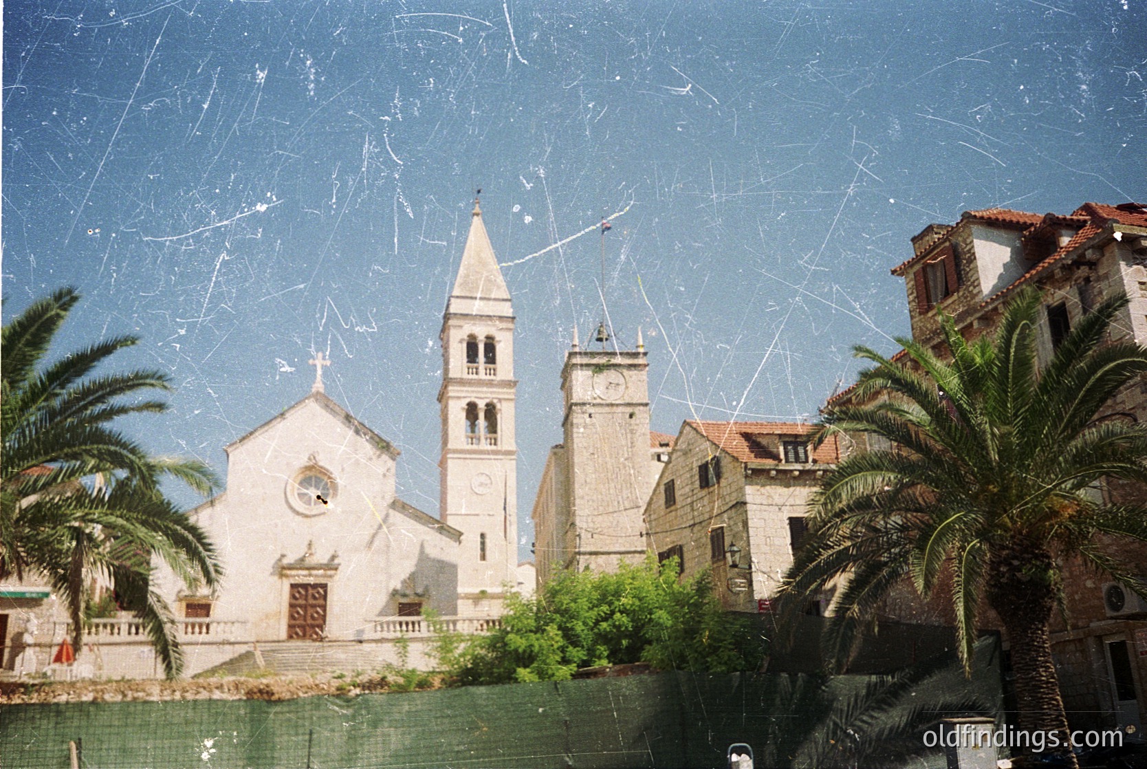 Vintage photograph of a Mediterranean coastal church with a prominent bell tower and arched windows, framed by palm trees and aged film grain. Likely *(Note: Specific location cannot be confirmed, but architectural style suggests Southern Europe.)*