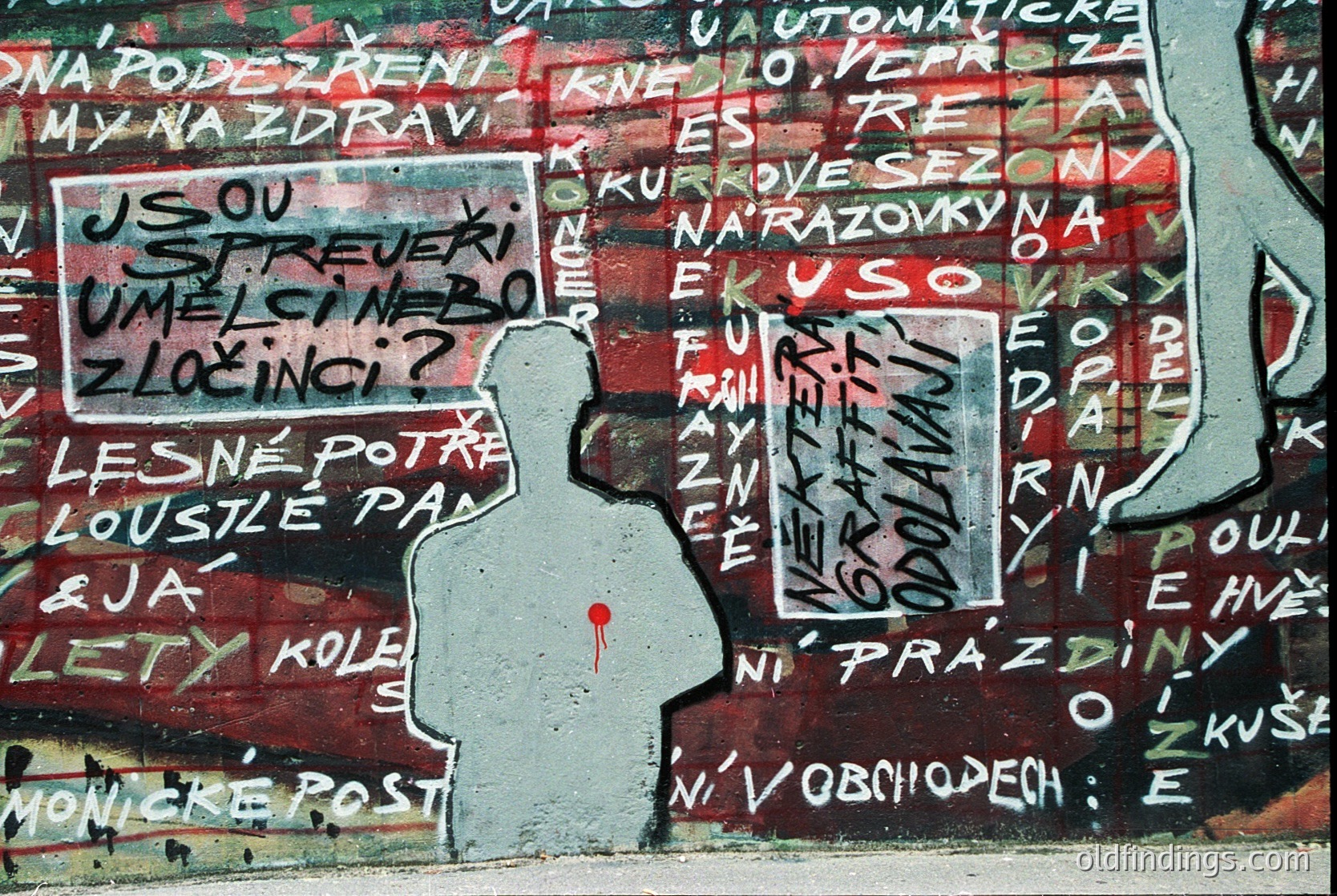 Graffiti mural featuring a black silhouette of a person with a red heart over their chest, set against a faded, red-painted wall. Text in Czech includes phrases like *"Jsou střežci umělců zločinci?"* and *"Lesné potře"*—suggesting themes of artistic freedom and protest. Likely from **Czech Republic**, **1980s–1990s** (dissident era).