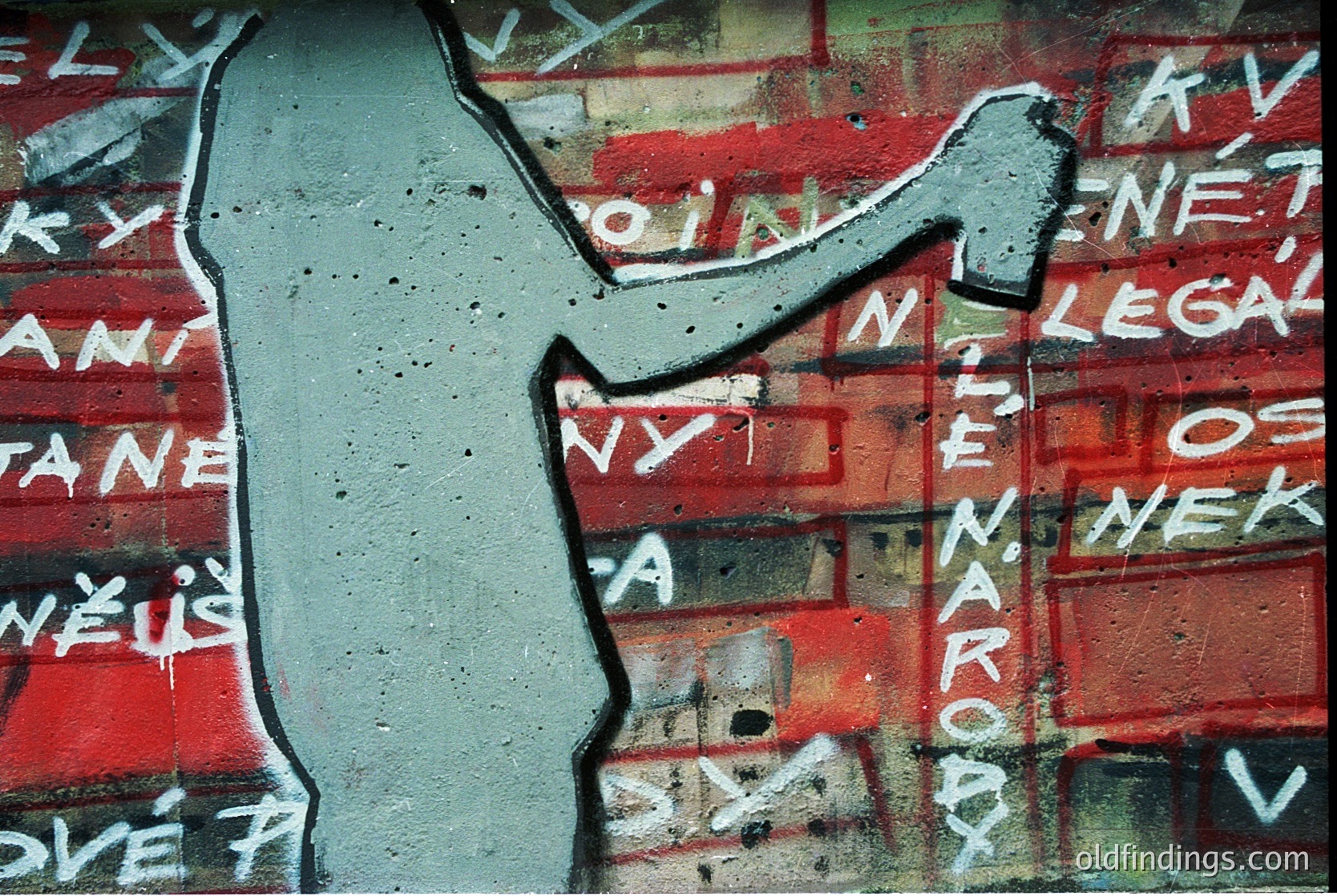 Stencil-style graffiti on weathered brick wall: bold white outline of a hand holding a hammer, with red-painted text in Czech ("Není legal osud národů" = "The fate of nations isn't legal"). Peeling paint and cracked plaster reveal layers of urban decay. Likely 2000s–2010s, Eastern Europe.