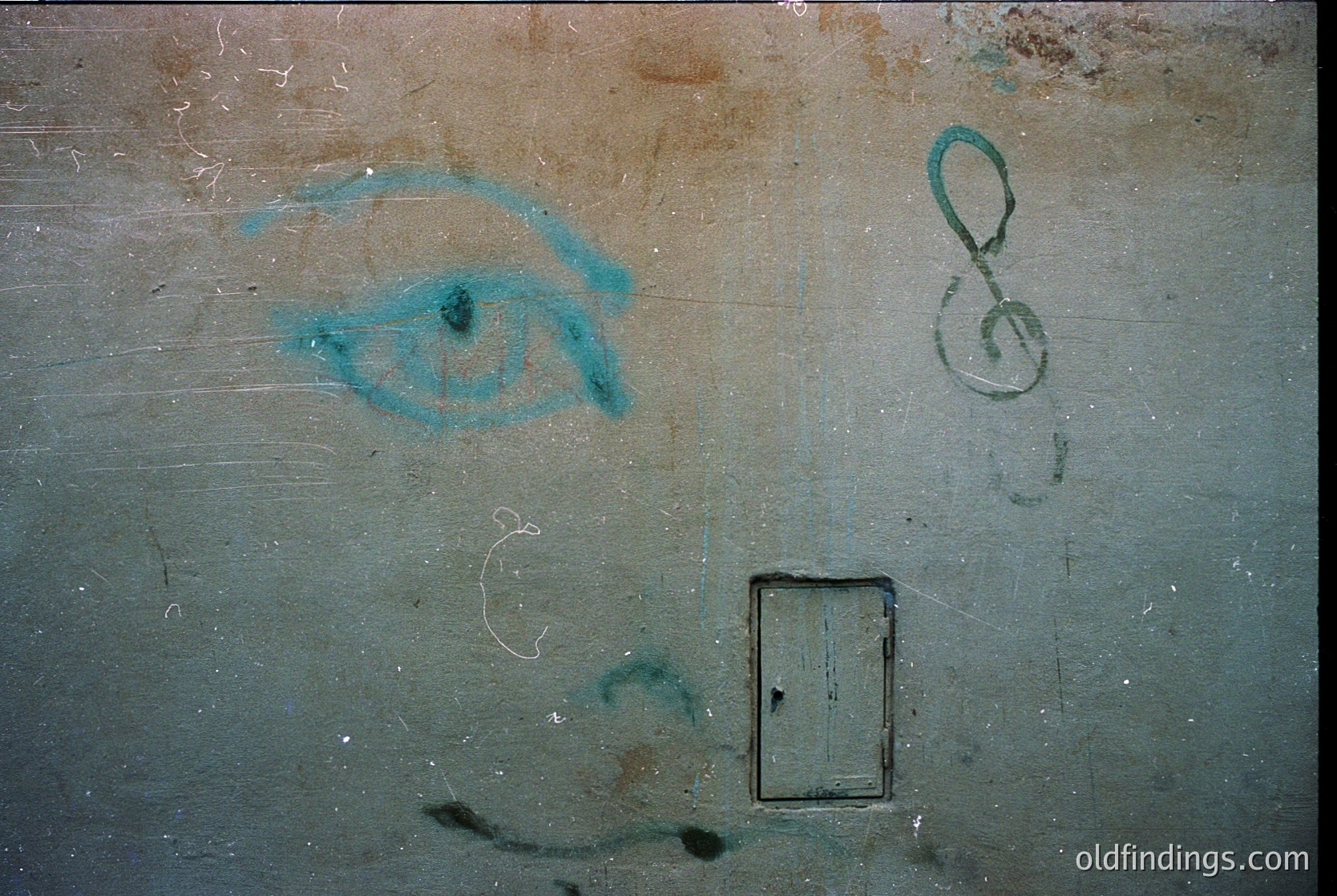 Graffiti of a stylized eye and treble clef symbol on aged, weathered concrete wall. Minimalist design with faded turquoise paint. Rectangular vent below. Evokes themes of surveillance and music. Potential urban decay or abandoned space.