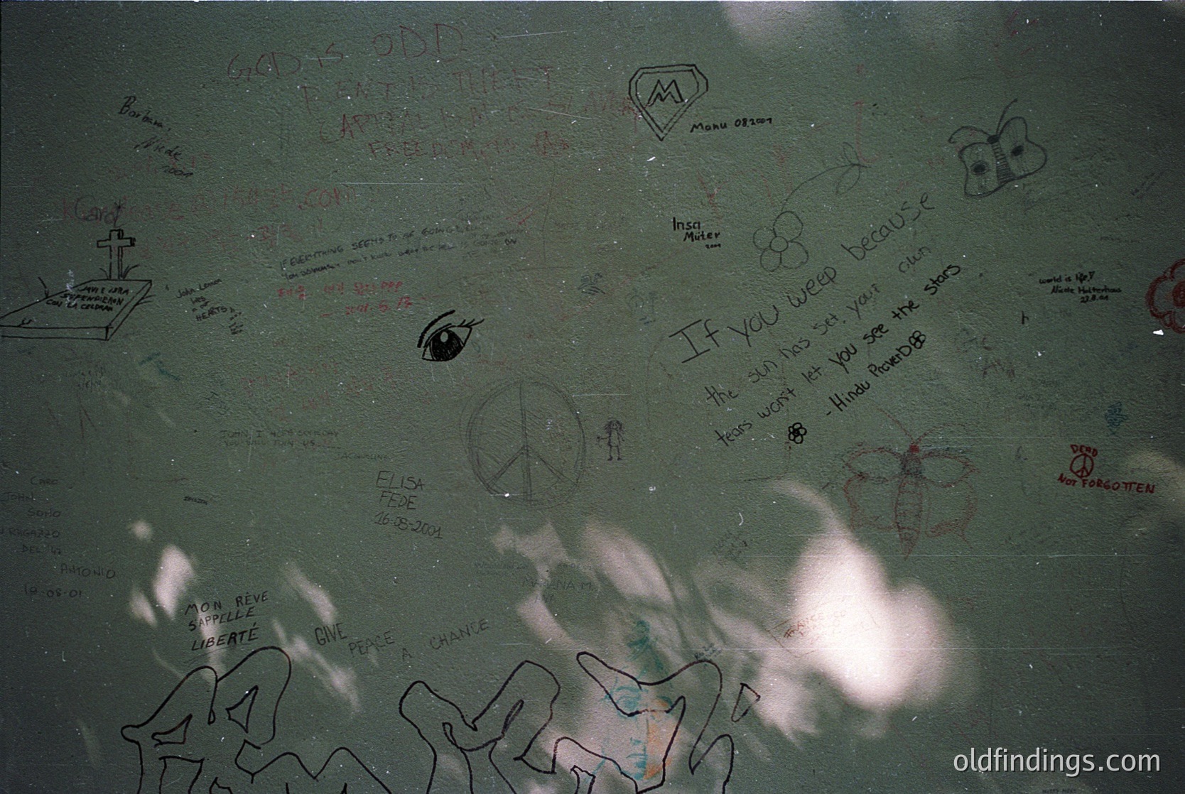 A close-up of a concrete surface covered in graffiti from the 1970s–1980s, featuring peace symbols, handprints, and messages like *"If you need me you're the one"* and *"Art is everywhere."* Includes a small cross and a stenciled butterfly. Likely urban/suburban setting.