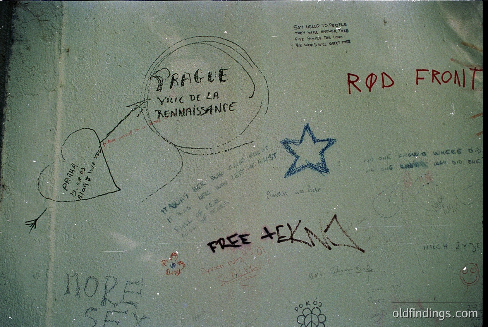 Graffiti-covered metal surface with handwritten messages in various styles, including "Prague Ville de la Renaissance," "Rod Front," "FREE TEKNI," and a blue star. Likely from Cold War-era Eastern Bloc travel documentation or a similar context.