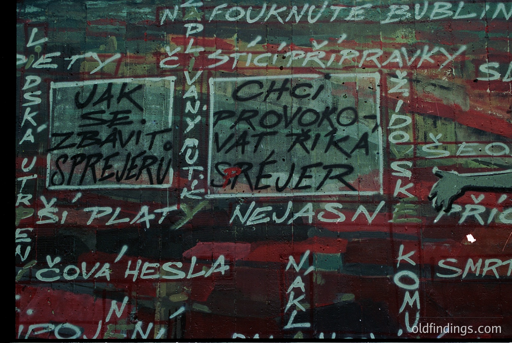 Vibrant graffiti on weathered concrete wall with Czech/Slovak text. Prominent phrases include *"CHCI PROVOKOVAT RÍKU"* ("I want to provoke the river") and *"SPREJER"* ("spray"). Peeling paint reveals faded red, green, and white layers. Likely urban street art from the late 20th century (). Evokes themes of rebellion and artistic expression.