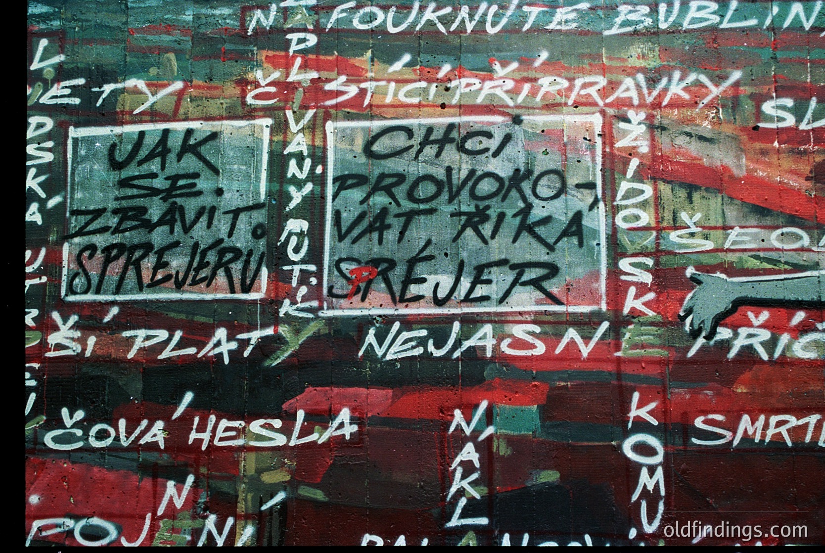Vibrant graffiti-covered wall with faded red paint and layered stenciled text in multiple languages (Czech, Slovak, Russian). Prominent phrases include *"CHCI PROVOKOVAT RIKA STREJER"* and *"NEJASNÉ SPREJERUJÍ."* Likely from a 1980s–1990s Eastern Bloc urban setting.