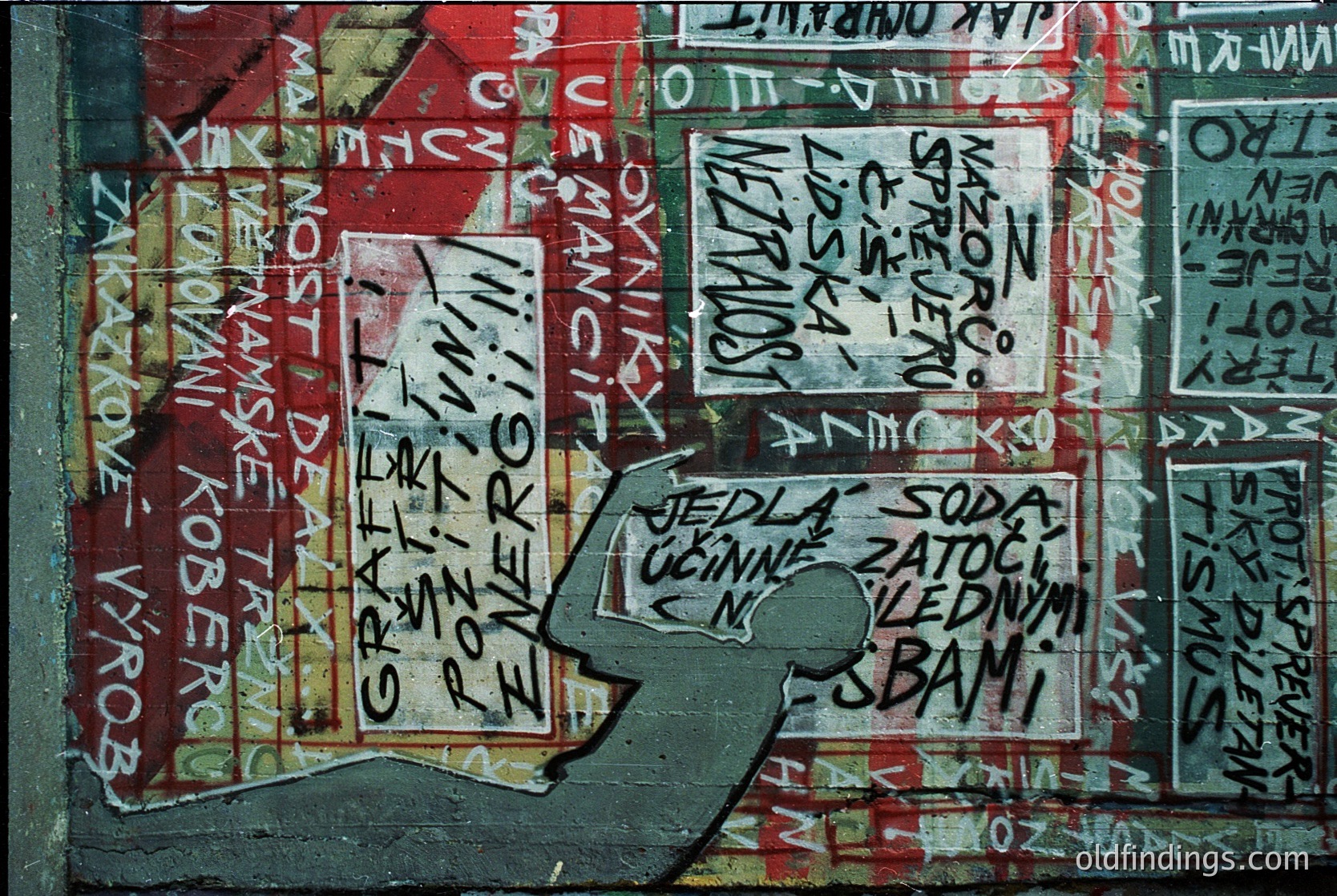 Vibrant graffiti-covered wall featuring layered Cyrillic text in red, white, and black ink. Prominent phrases include *"Jedla, pila, kouřila, spala, šla do práce"* ("Ate, drank, smoked, slept, went to work") and *"Soda Zlatý slon"* ("Golden Elephant Soda"). Decayed poster fragments and faded advertisements add texture. Likely Eastern European urban setting, 1980s–1990s.