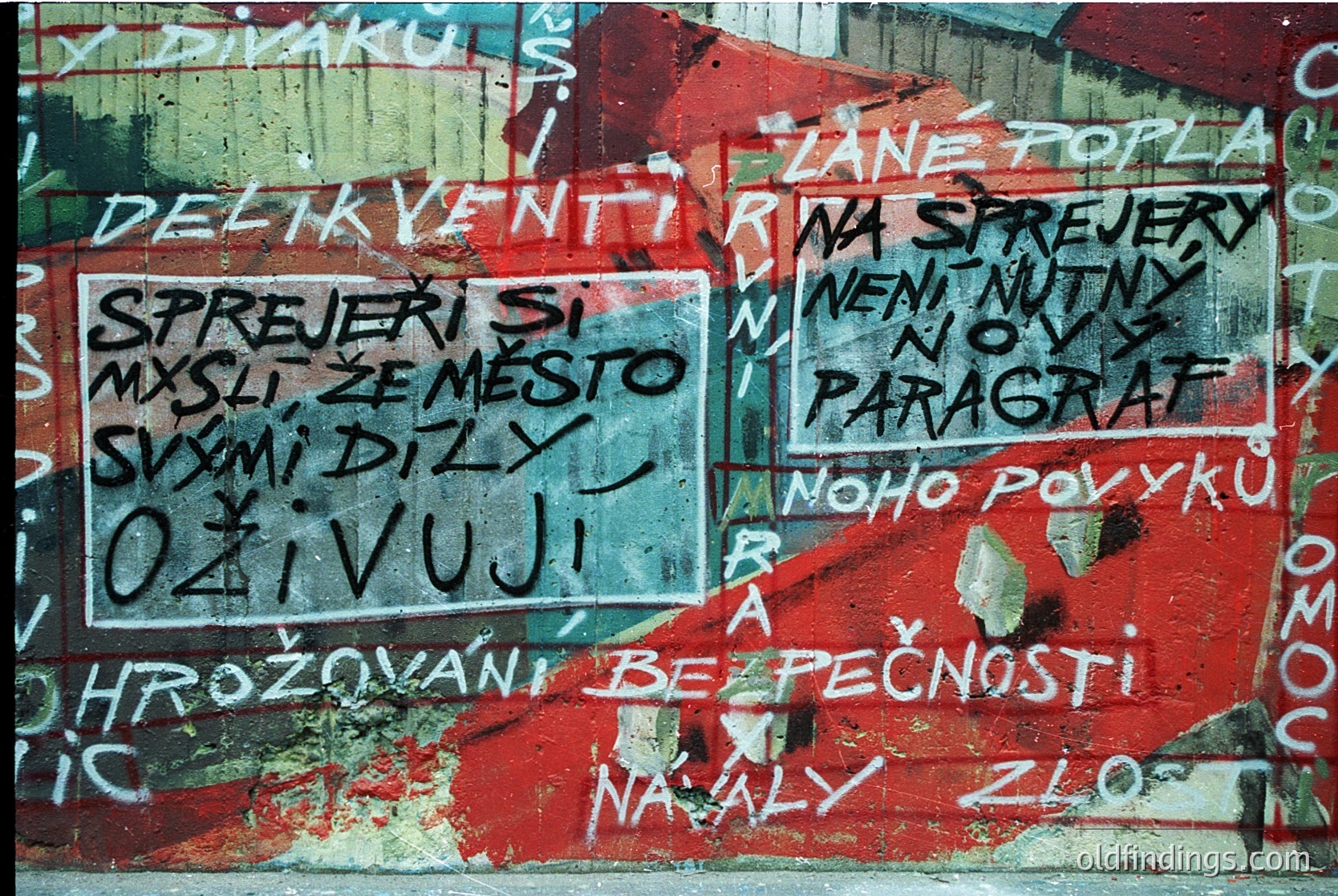 Graffiti on weathered concrete wall with Czech/Slovak text criticizing corruption and political hypocrisy. Bold phrases like *"Sprejery si myslí že město suší dílny ožívují"* and *"Neni nový paragraf"* suggest civic discontent. Peeling paint and faded colors indicate age, likely 1980s–1990s Eastern Bloc era. Urban decay and political commentary make this valuable for historical research.