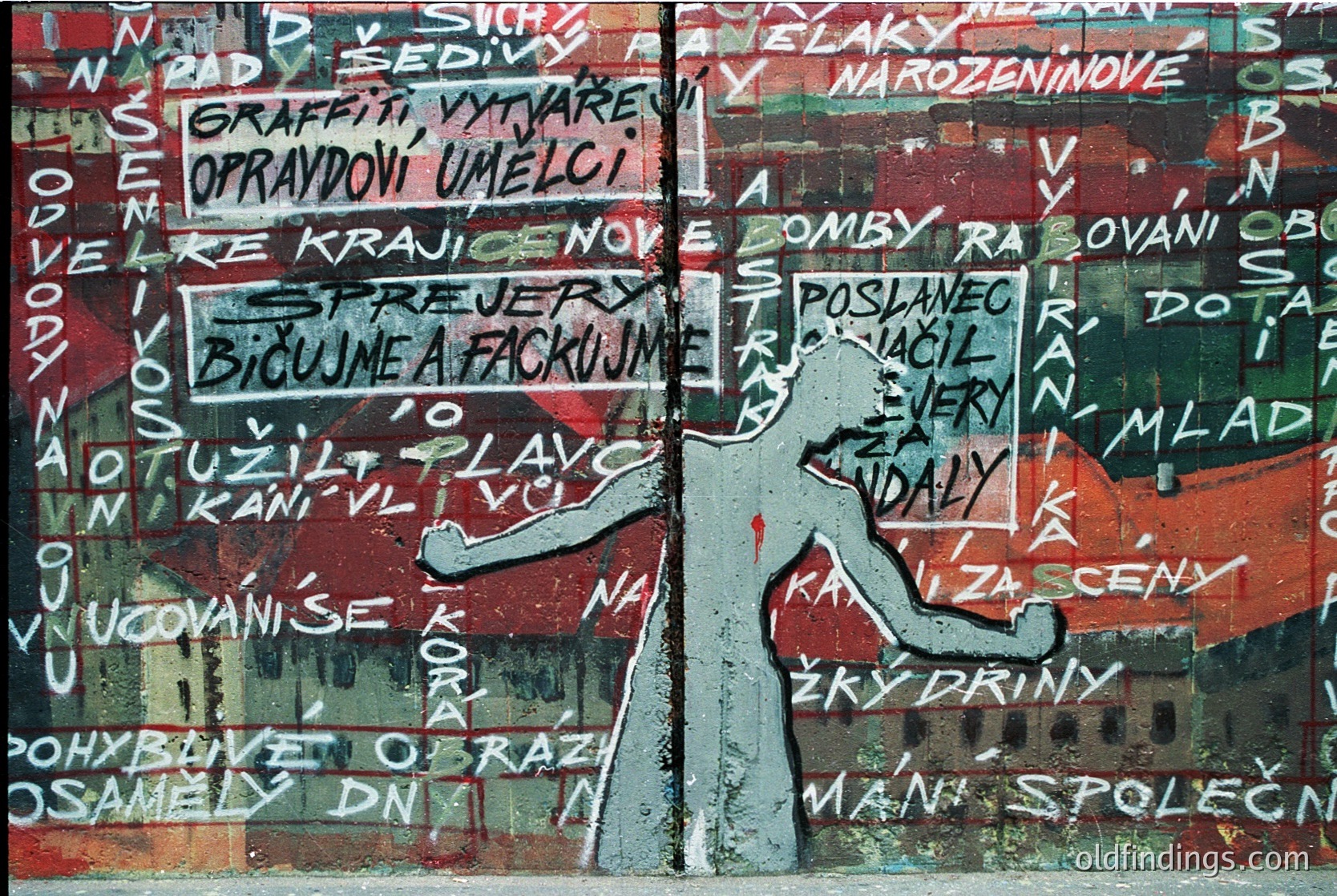 Vibrant street mural featuring bold, layered graffiti in Czech with a central silhouette of a person in motion. Text includes phrases like *"Graffiti umělci"* (graffiti artists) and *"Bídujeme a fackujeme"* (we suffer and f*ck). Peeling paint reveals faded red and white underlayers. Likely 1980s–1990s Prague, capturing dissident art during communist era.