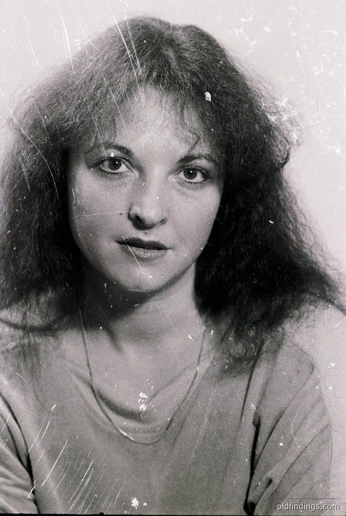 Black-and-white portrait of a woman with voluminous shoulder-length hair, shot in mid-20th century style. Her direct gaze and subtle makeup suggest a candid yet posed studio portrait. The grainy texture and lighting indicate or photography.