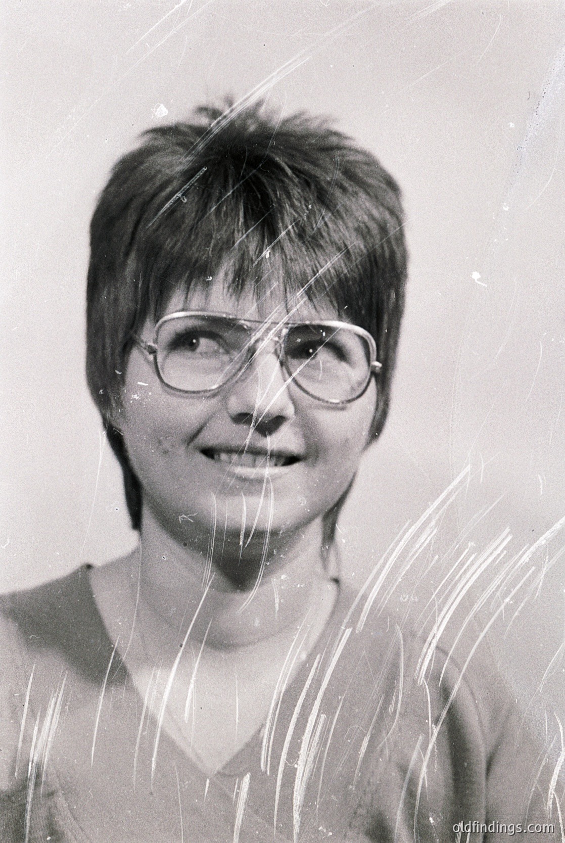 Portrait of a person with short, layered hair and round glasses, captured mid-shower with water droplets on their face and shoulders. The image suggests a candid, everyday moment from the 1970s–1990s. Style reflects mid-century household photography.