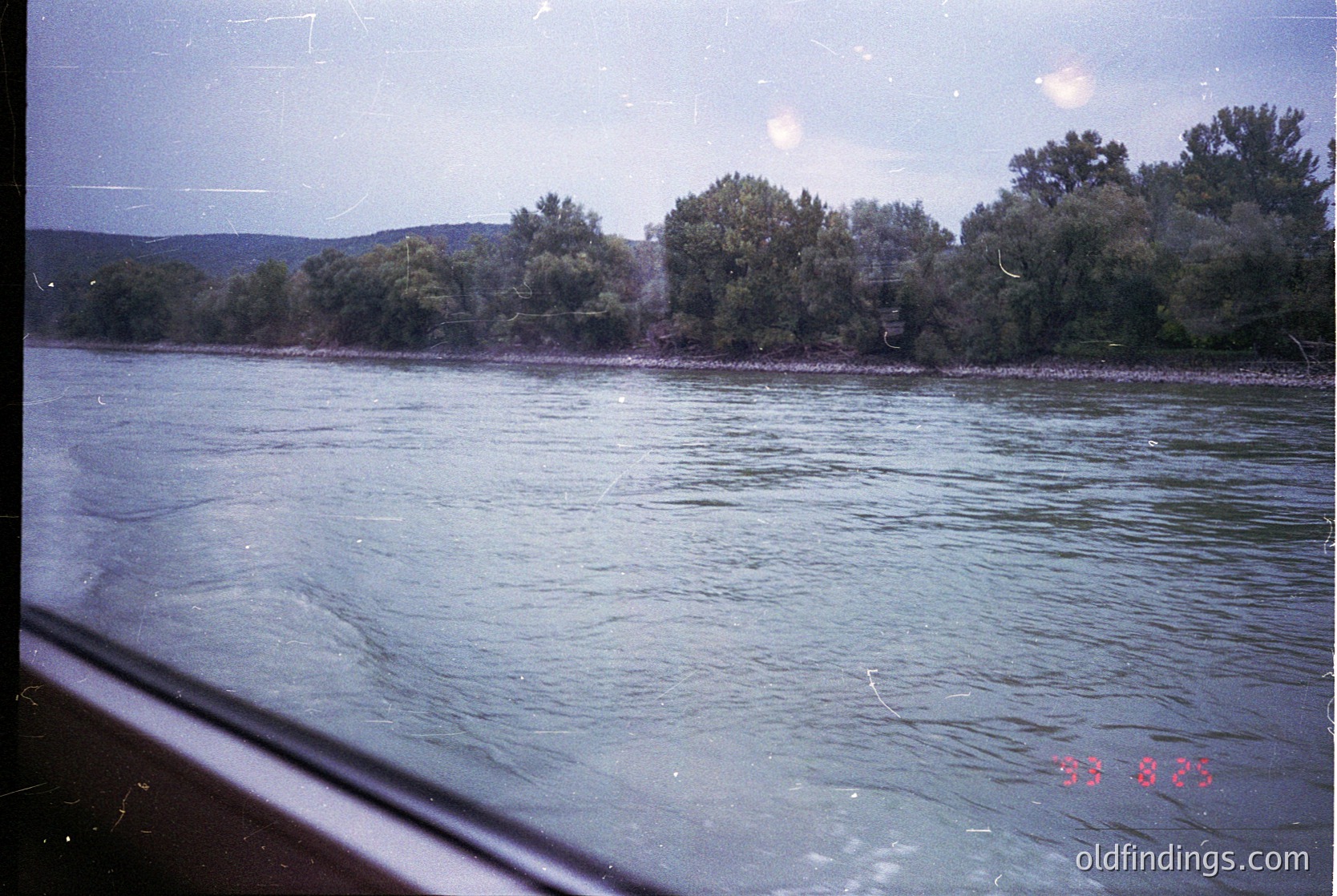 Vintage riverbank scene with dense greenery and rippling water, viewed from a vehicle window. Overcast sky and blurred foreground suggest motion. Stamp "33 825" indicates possible archival or travel documentation. Likely mid-20th century.