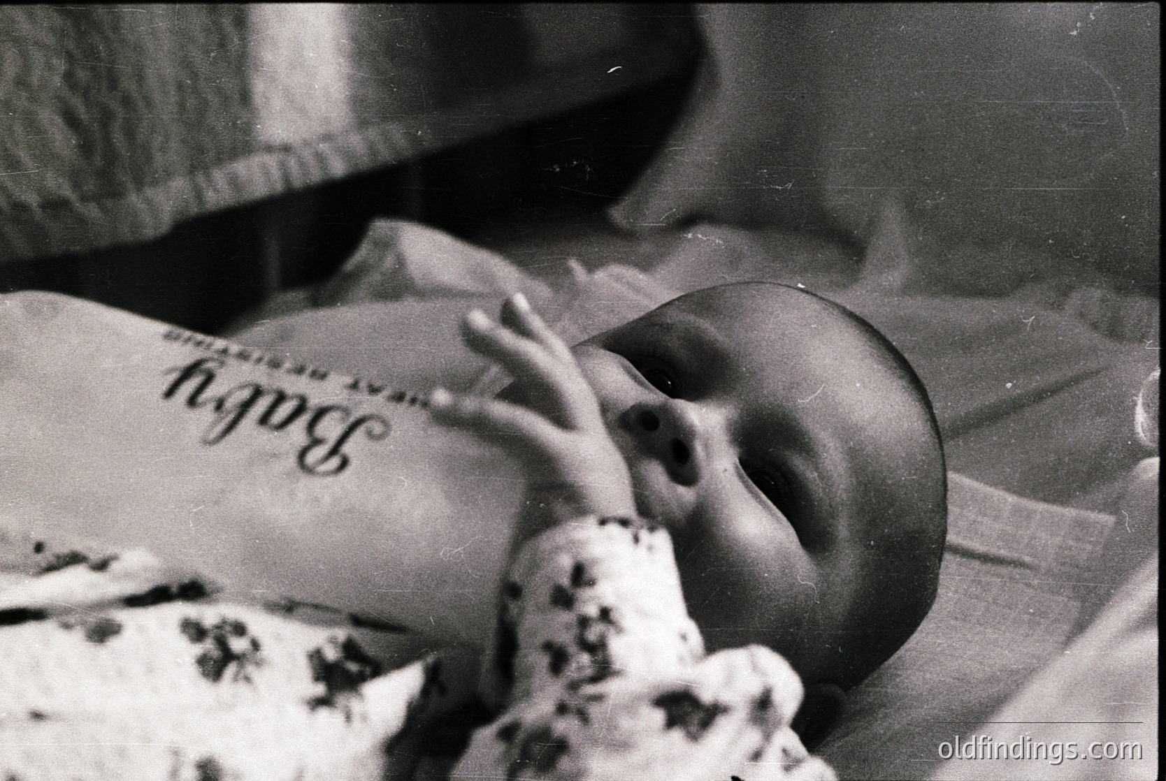 Black-and-white portrait of an infant swaddled in a blanket with "Baby" and "Resident" printed on it, likely from a 1950s–1970s hospital. Soft focus captures tender moment of sleep or rest. Ideal for historical research on pediatric care or vintage family archives.