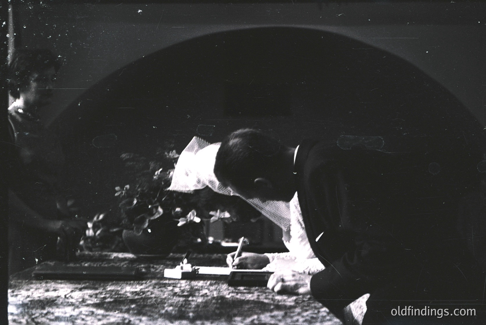 Vintage black-and-white portrait of a man engrossed in writing at a desk, likely mid-20th century. Formal attire (vest, tie, cap) suggests a professional or academic setting. Distressed film grain and lighting enhance nostalgic vintage aesthetic.