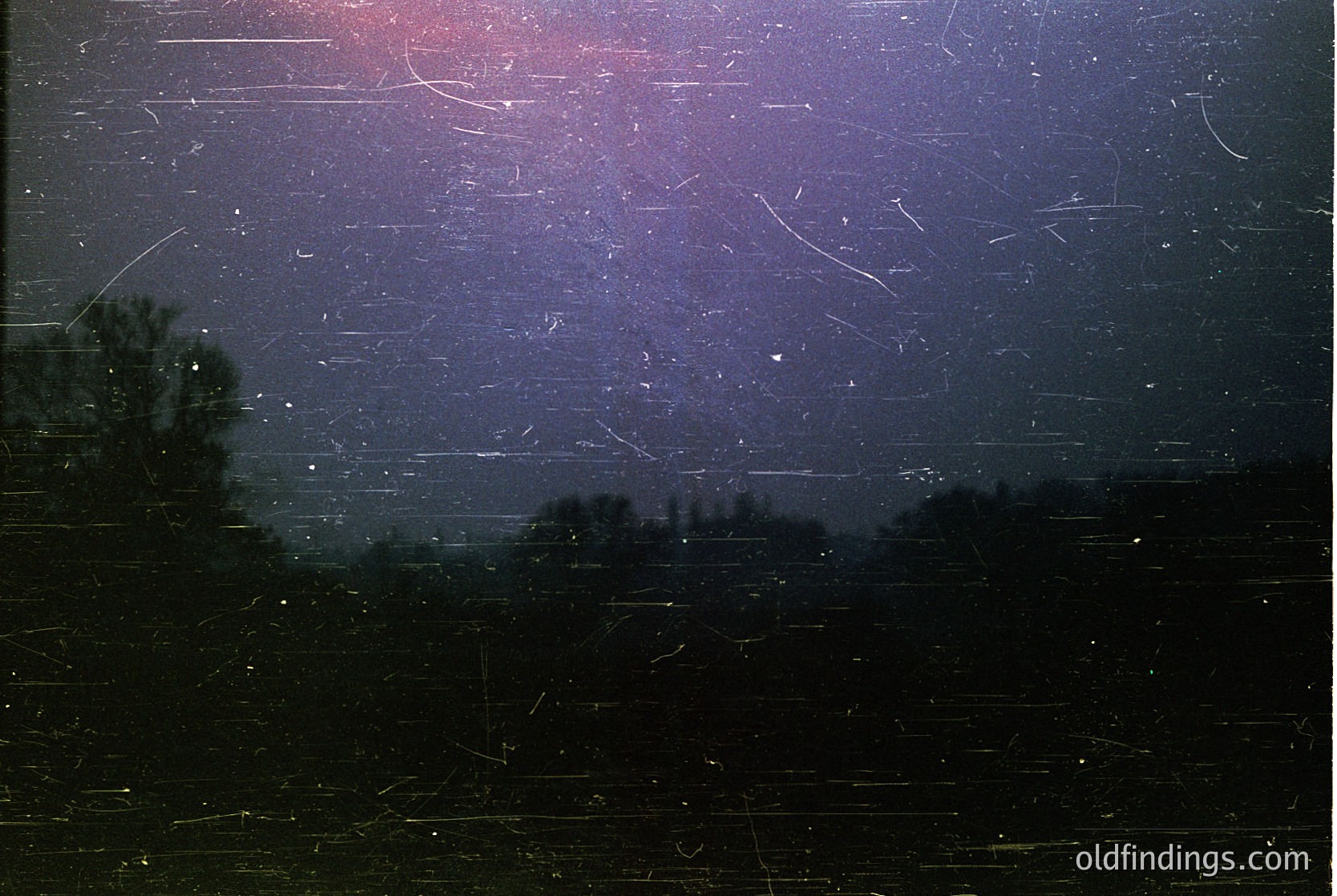 Vintage film capture of a starry night sky with faint, streaked light trails—likely from long exposure. Silhouetted trees frame the horizon. Artistic grain and faded tones suggest mid-20th century photography (). Ideal for moody, atmospheric stock or film-inspired design.