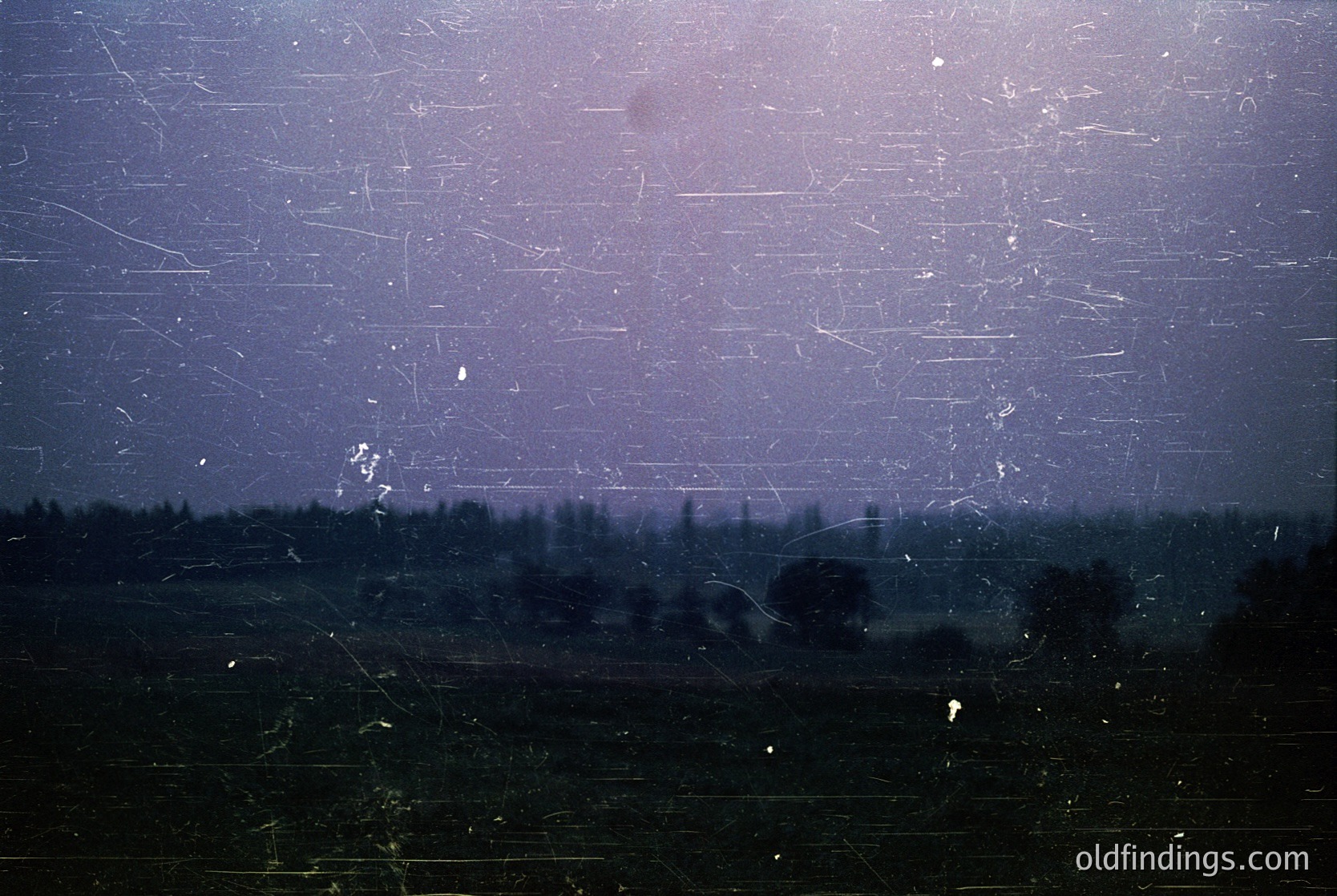 Vintage photograph showing a cracked, foggy windowpane with blurred forest and fields beyond. Heavy scratches and condensation obscure details, suggesting an aged or damaged slide/film. Likely 20th-century rural European setting.