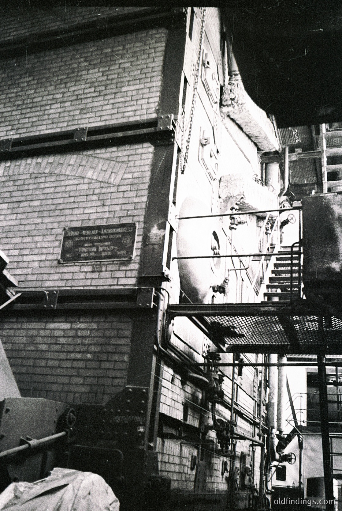 Industrial brick stairwell with exposed pipes, scaffolding, and a plaque reading *"The Old Factory"* (likely Soviet-era or Eastern Bloc). Rustic concrete steps and metal railings contrast with worn plaster. Mid-century Soviet industrial architecture ( )