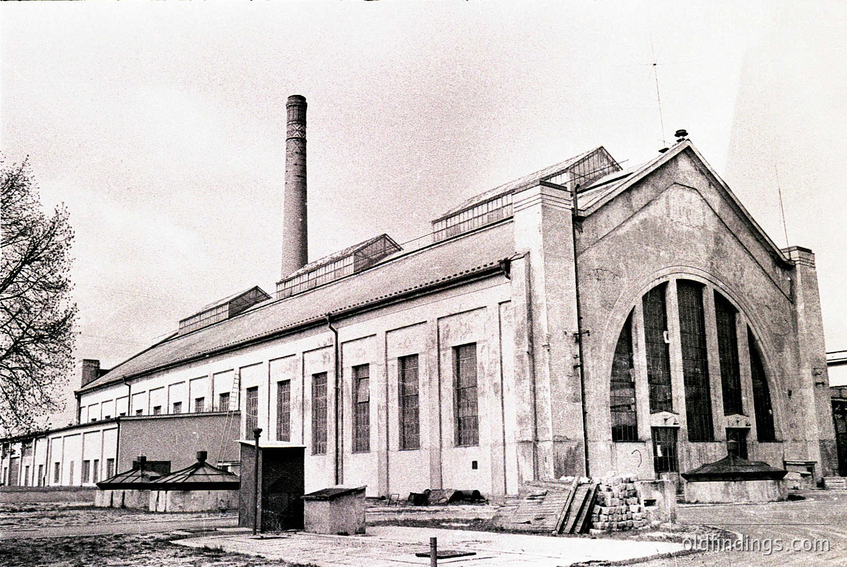 Industrial-era brick building with Art Deco architectural elements, featuring a tall chimney and arched entrance. Signage suggests it may have been a power plant or factory. Mid-20th century, likely Eastern European.