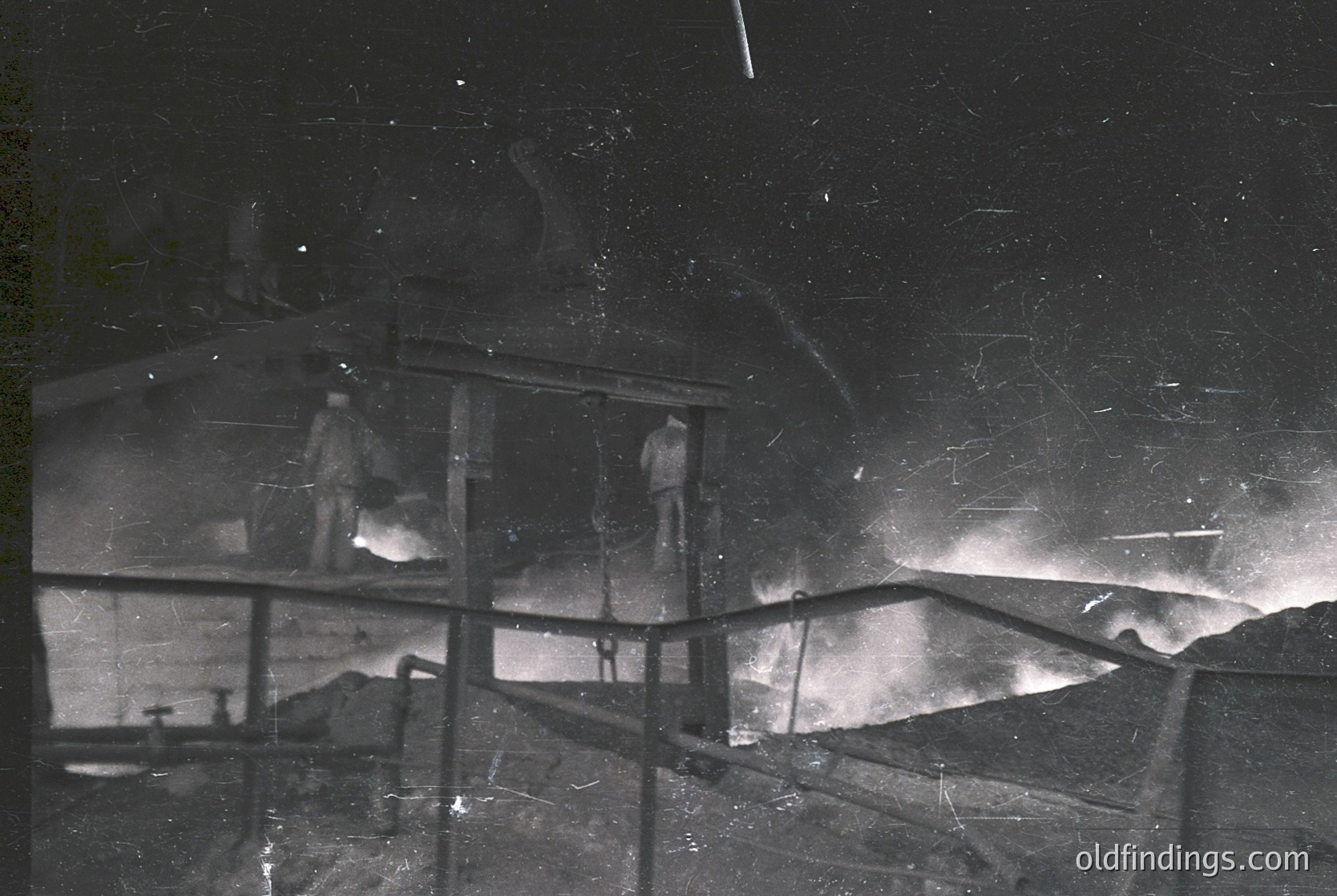 Vintage black-and-white photo of a **mining or industrial site** at night, featuring a **suspended platform** with two workers. The **star-strewn sky** and **flickering light** suggest a remote, high-altitude location. Likely **1940s–1960s** era, possibly **Alpine or Arctic mining** operations.