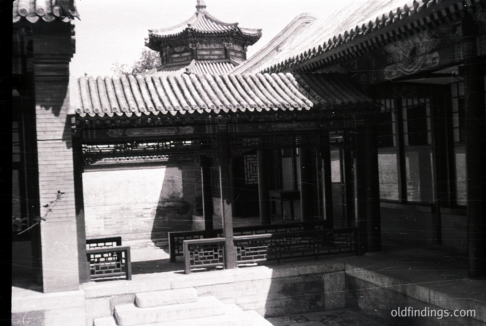 Traditional Chinese courtyard with upturned eaves and tiled roofing, likely from the early-to-mid 20th century. Stone-paved entranceway leads to a wooden-paned windowed building. Architectural details include ornate wooden brackets and tiled walls.