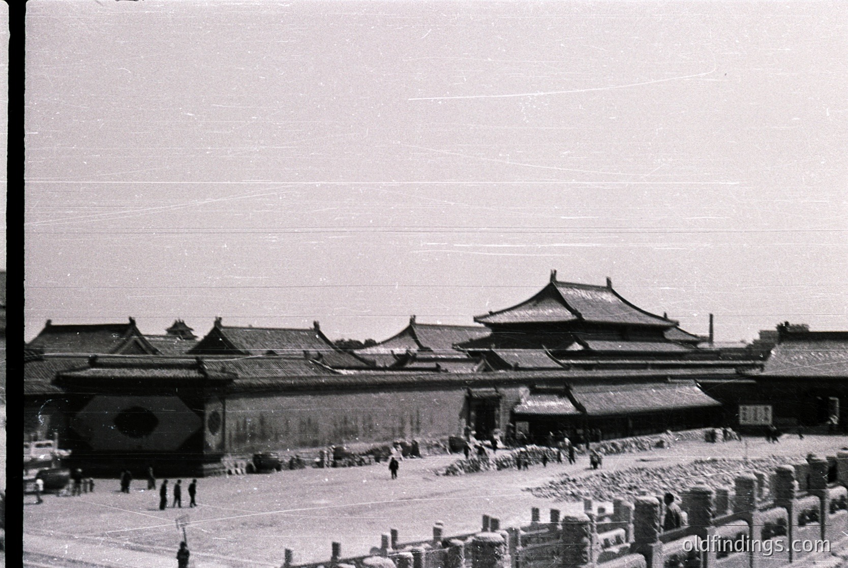 Black-and-white photograph of the Forbidden City’s **Tiananmen Gate** and courtyard, showcasing traditional Chinese imperial architecture with upturned eaves and tiled roofs. Crowds of people in mid-20th-century attire gather near the gate’s iconic circular and square holes. The scene reflects the cultural and historical significance of Beijing’s Forbidden City ( ).