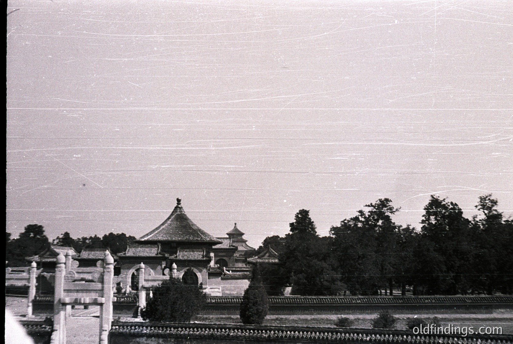 Vintage black-and-white photo of traditional Chinese pavilion with upturned eaves, surrounded by dense greenery and a low stone wall. Likely 20th-century architecture, possibly or due to style.