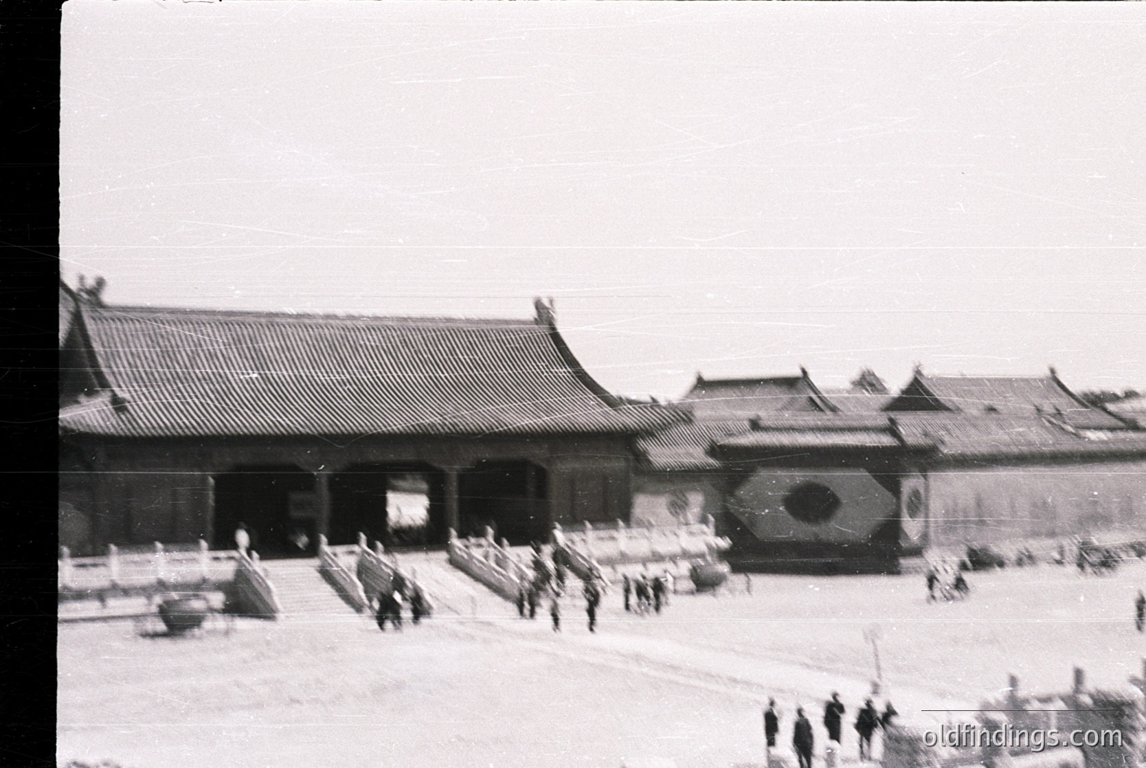 Black-and-white photograph of traditional East Asian palace courtyard with tiled roofs and ornate gateways. Uniformed guards and civilians in period attire walk through archways. Likely or early .