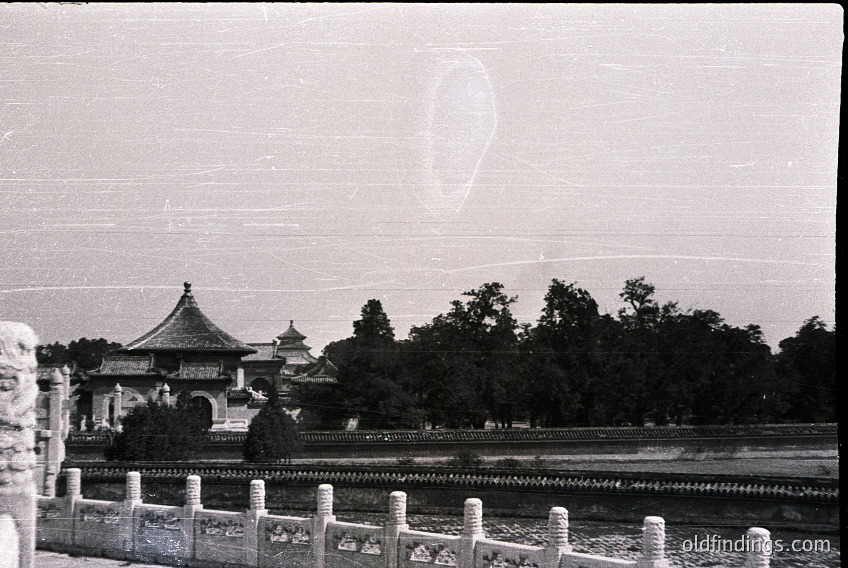 Vintage black-and-white photo of traditional Chinese pavilion with upturned eaves, set beside a stone bridge and lush greenery. Likely 20th-century architecture, possibly ’s . Classic design with serene waterfront setting.