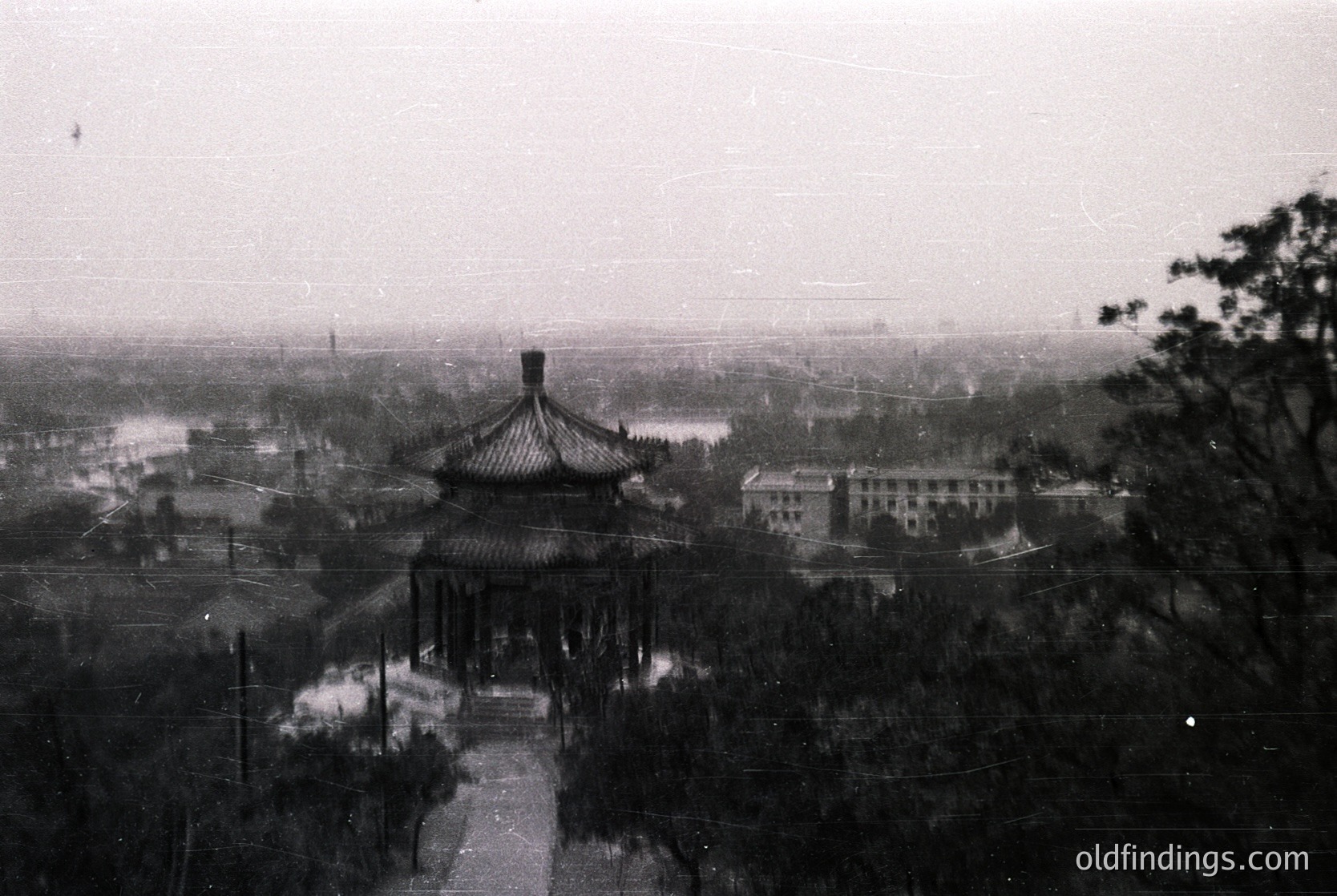 Classic Chinese pavilion with upturned eaves and curved roof ridges, framed by a winding path. Urban sprawl and water body in background, suggesting Beijing’s historical layout. Likely mid-20th century due to monochrome and architectural style.